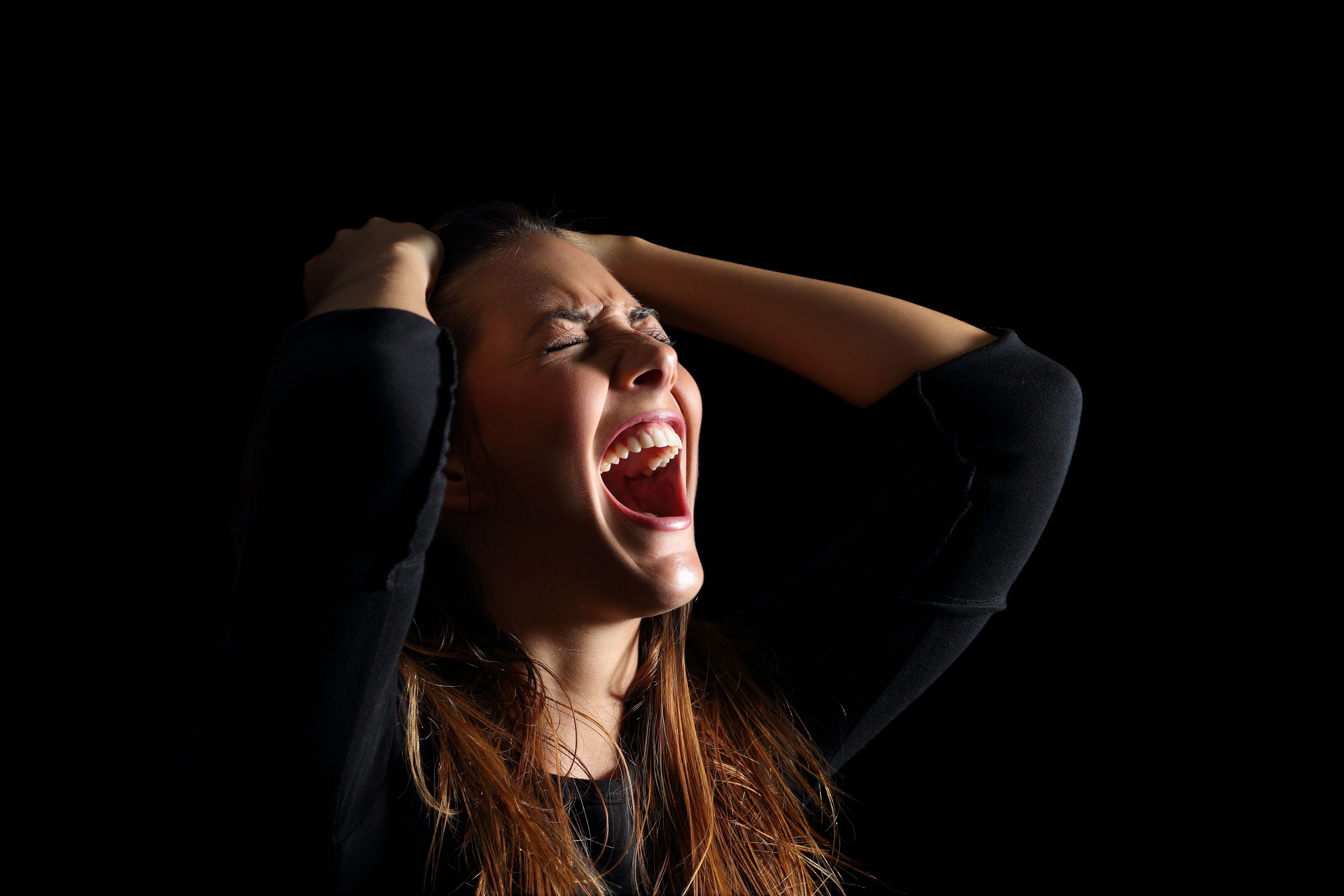 A woman with her eyes closed and screaming while holding her hair | Source: Getty Images