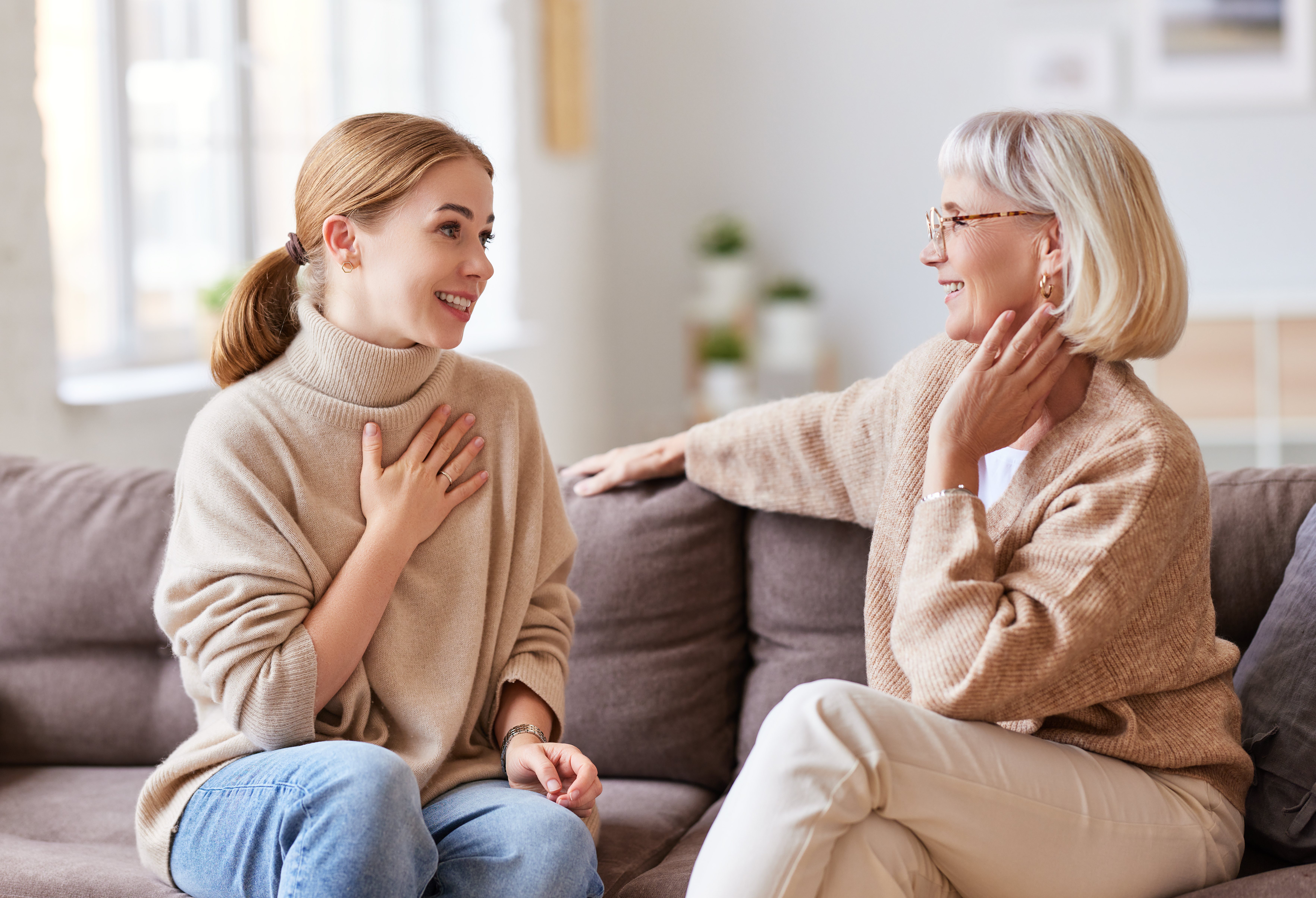A younger woman smiling while talking to an older one while seated on a couch | Source: Shutterstock