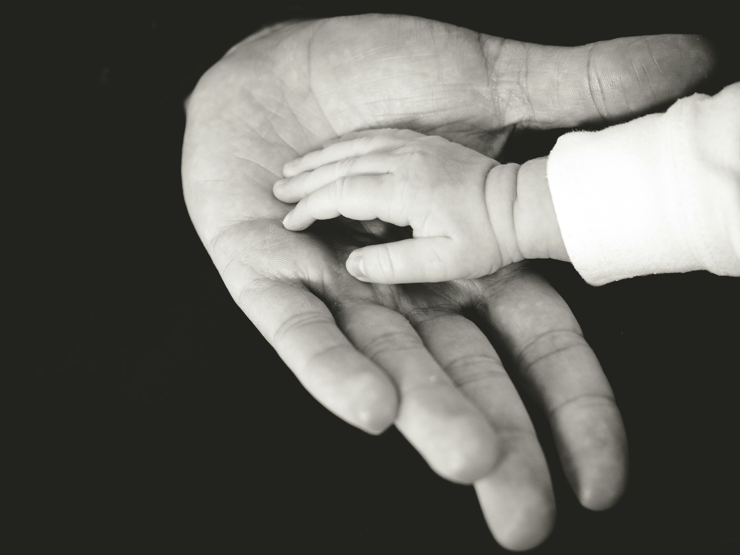 A grayscale photograph of a parent holding their baby's hand | Source: Unsplash