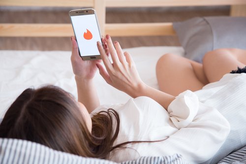 Mujer acostada revisando su cuenta de Tinder en su celular. | Foto: Shutterstock