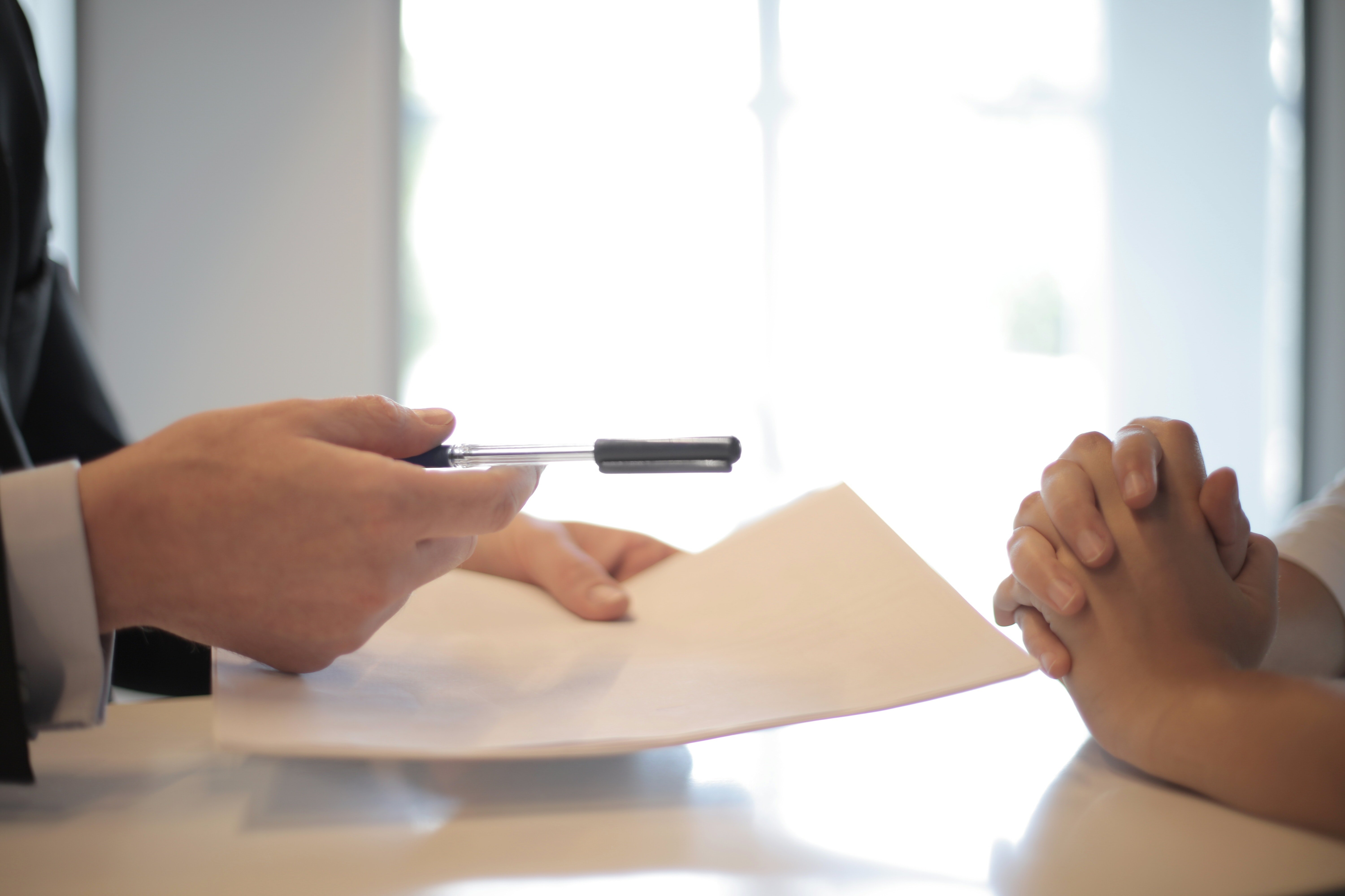 A person's holding a pen and extending a document to another person | Source: Pexels