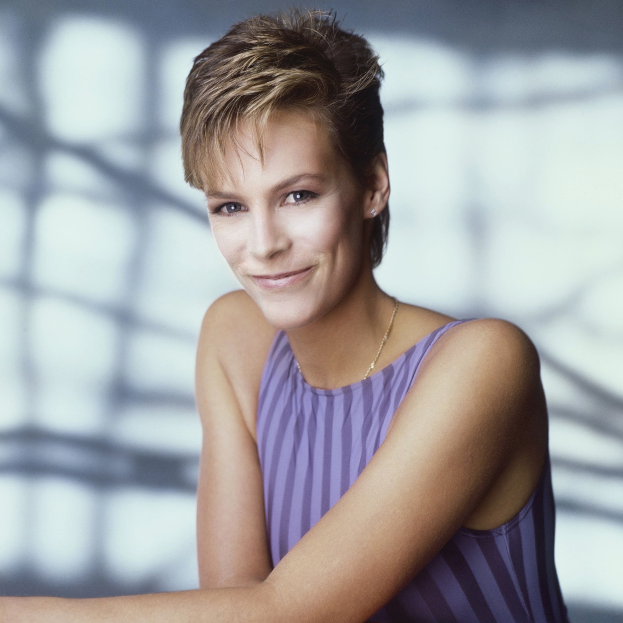 In a striking portrait session, Jamie Lee Curtis exudes confidence and charm in a sleeveless purple-striped top, showing off her signature pixie cut and effortless style.