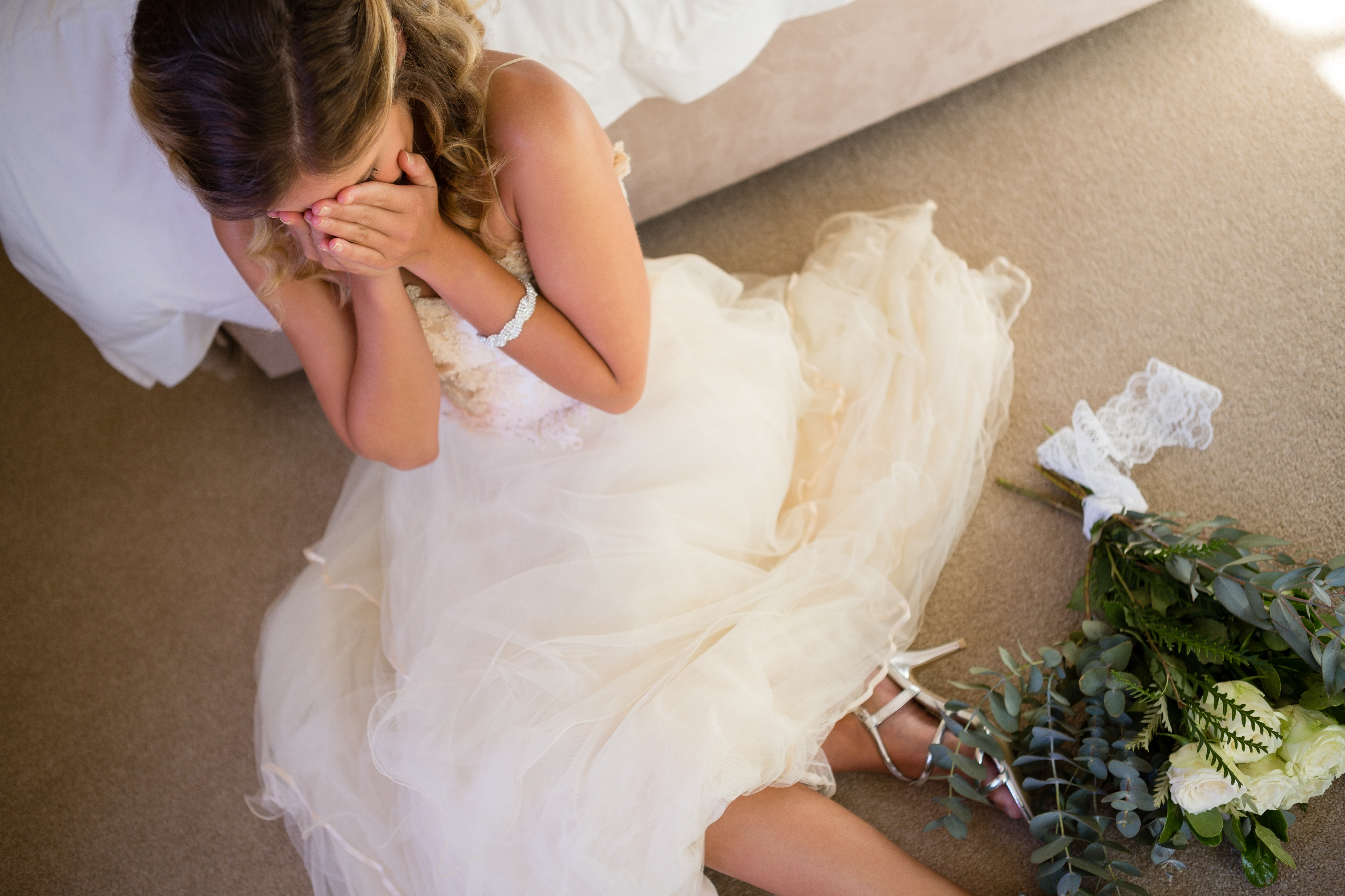 A bride crying on the floor as she leans on a bed | Source: Shutterstock