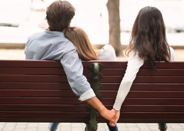 Ein Mann hält die Hände einer Frau, während er eng mit einer anderen zusammensitzt | Quelle: Pexels