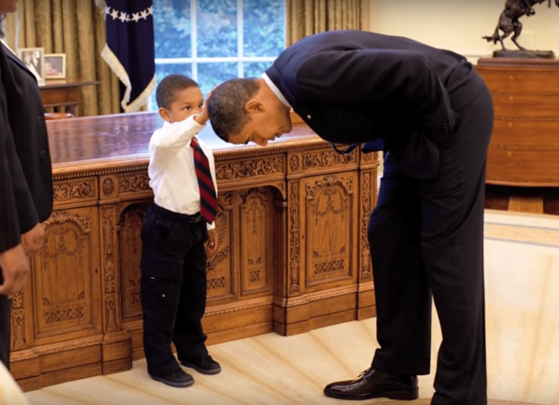 Obama bends down to let a young boy touch his head. | Source: YouTube/washingtonpost