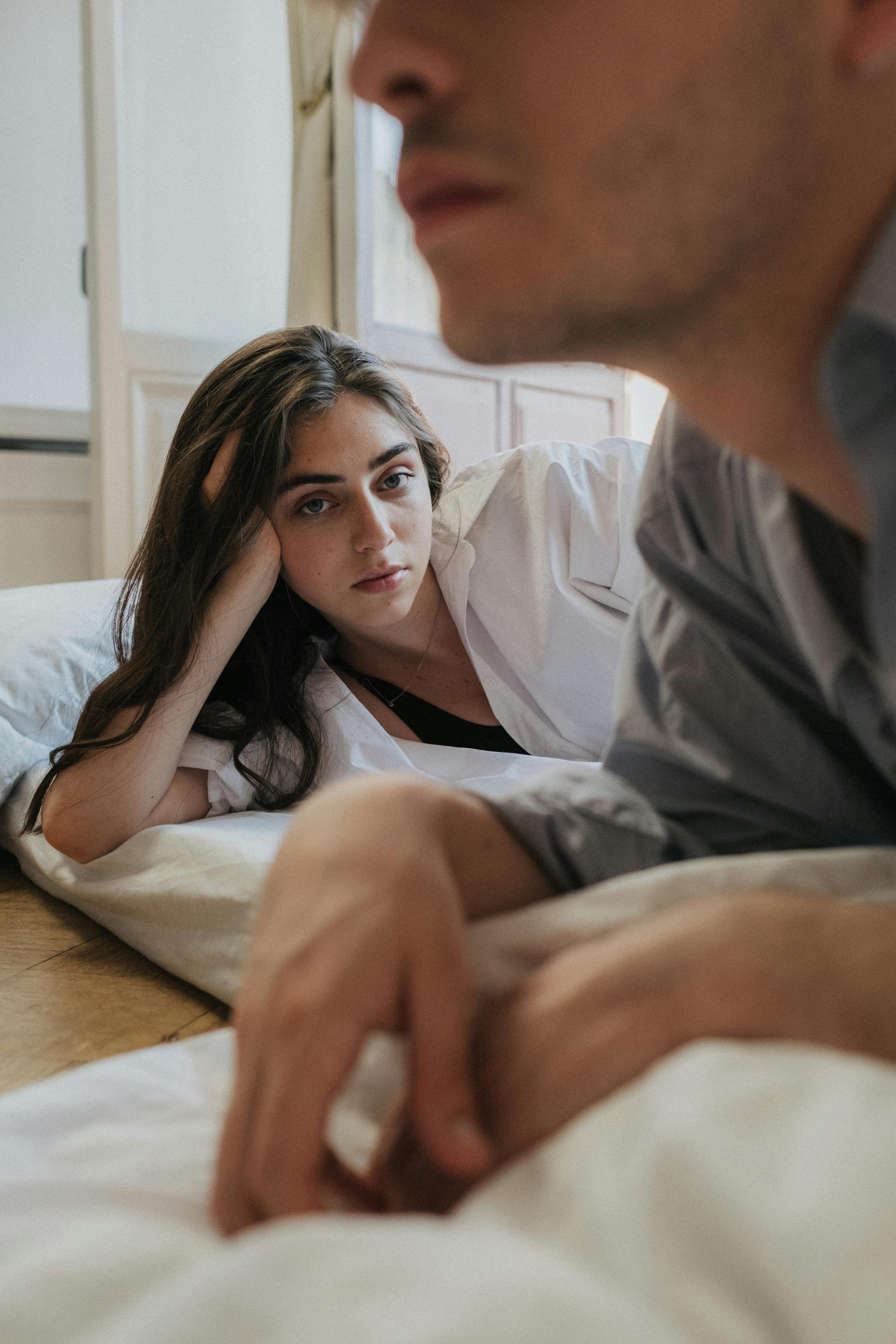 A woman looking distant while lying down next to her partner | Source: Pexels