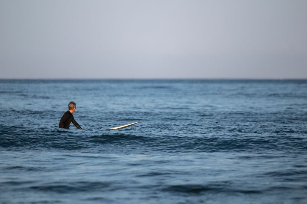 Un homme attend une vague sur sa planche de surf sur une plage.| Photo : Getty Images