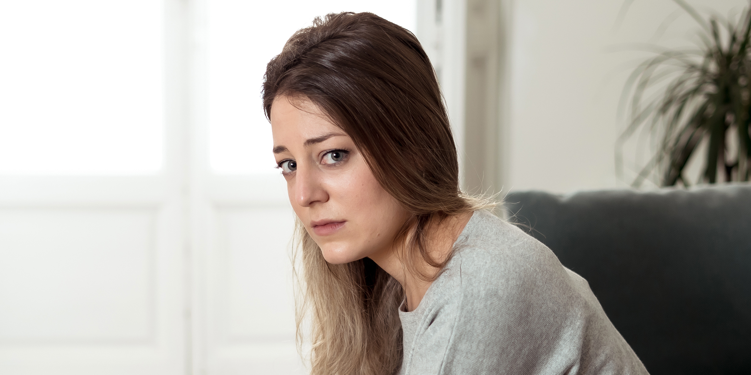 A sad-looking woman sitting home alone | Source: Shutterstock