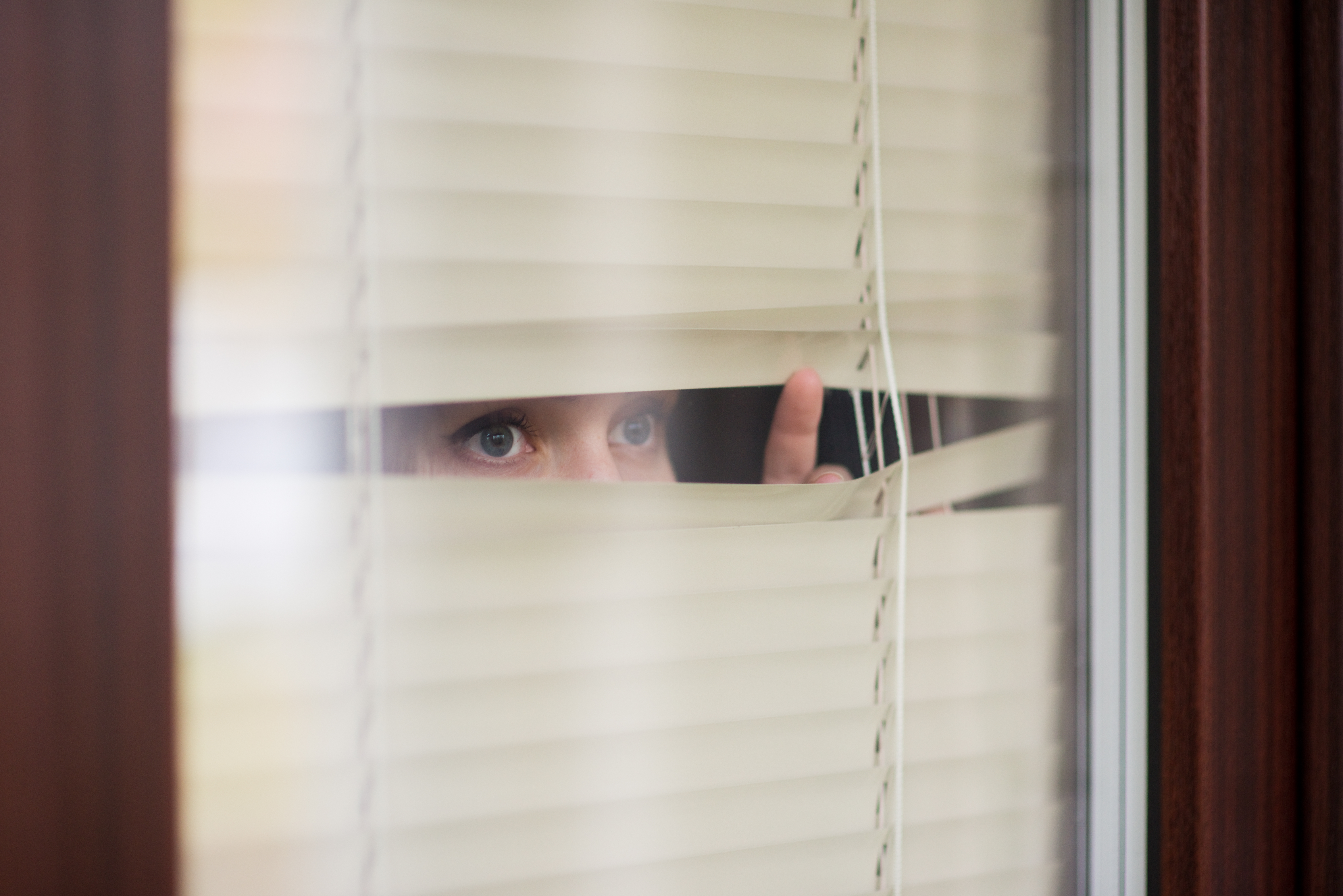 woman looking through window blinds into the street waiting, side view | Source: Shutterstock