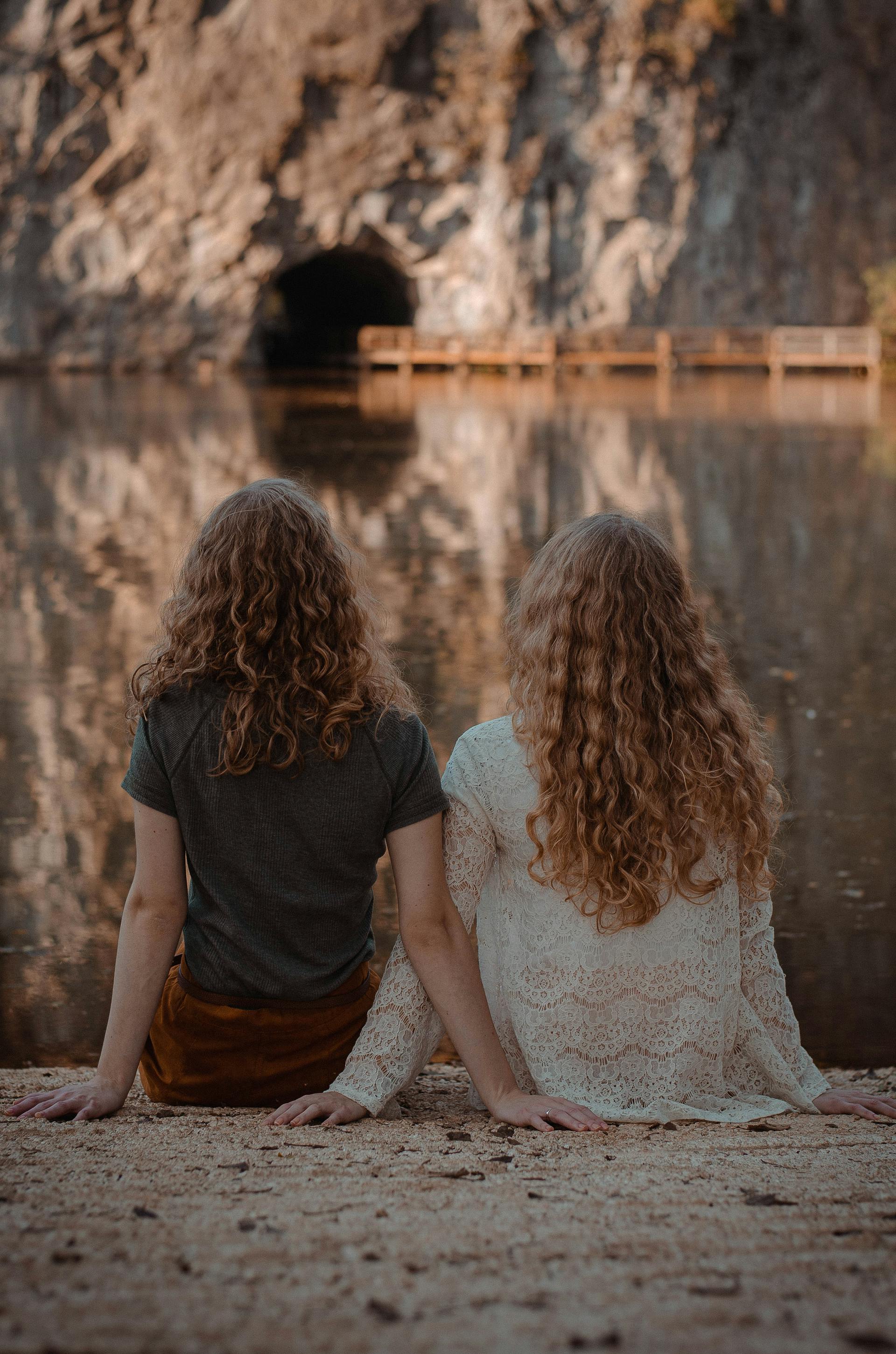 Two women sitting on the ground facing a water body | Source: Pexels