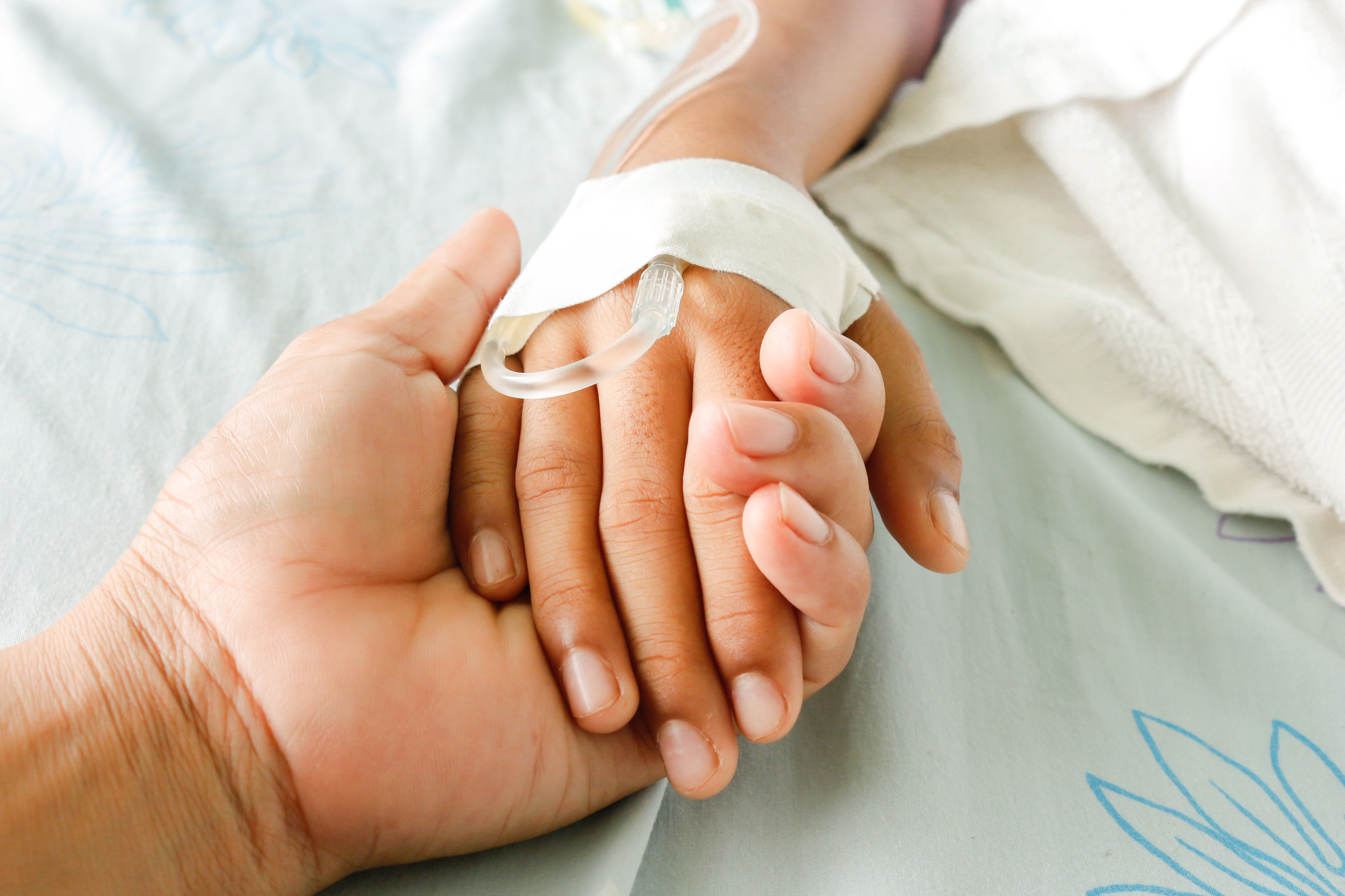 Madre sosteniendo mano de hija en cama de hospital. | Foto: Shutterstock