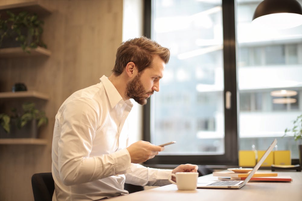 Un homme lisant un message texte alors qu'il était au bureau. | Pexels