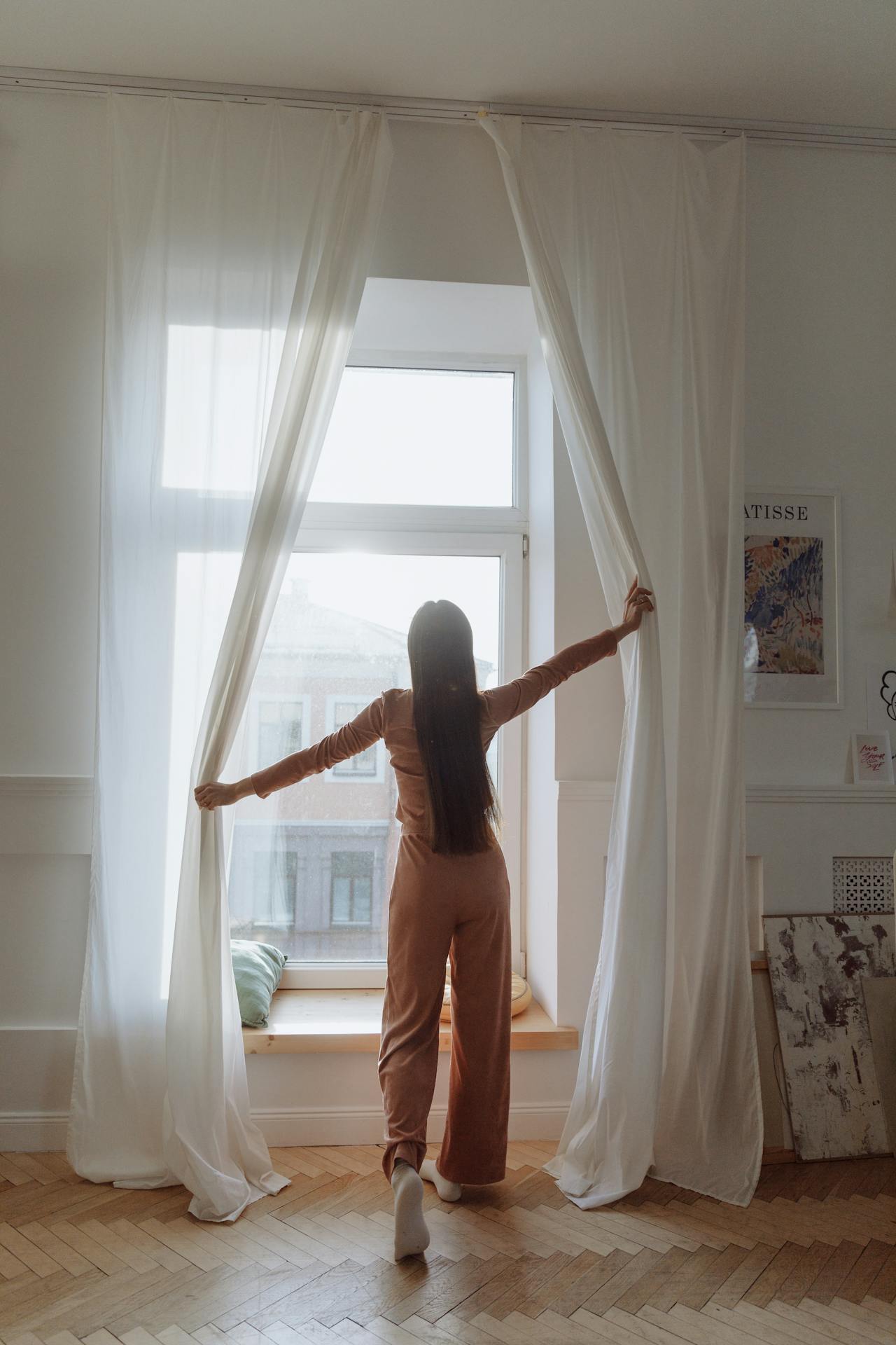 A woman standing near the window and opening the curtains | Source: Pexels
