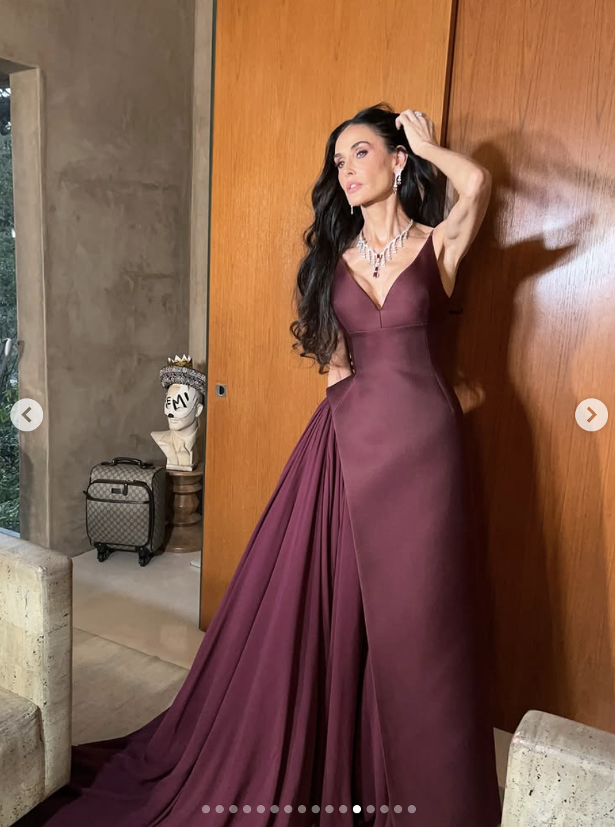 Striking a candid pose against a wood-paneled wall, Demi Moore channels high fashion drama in her flowing maroon gown, one hand swept through her hair mid-movement. | Source: Instagram/demimoore