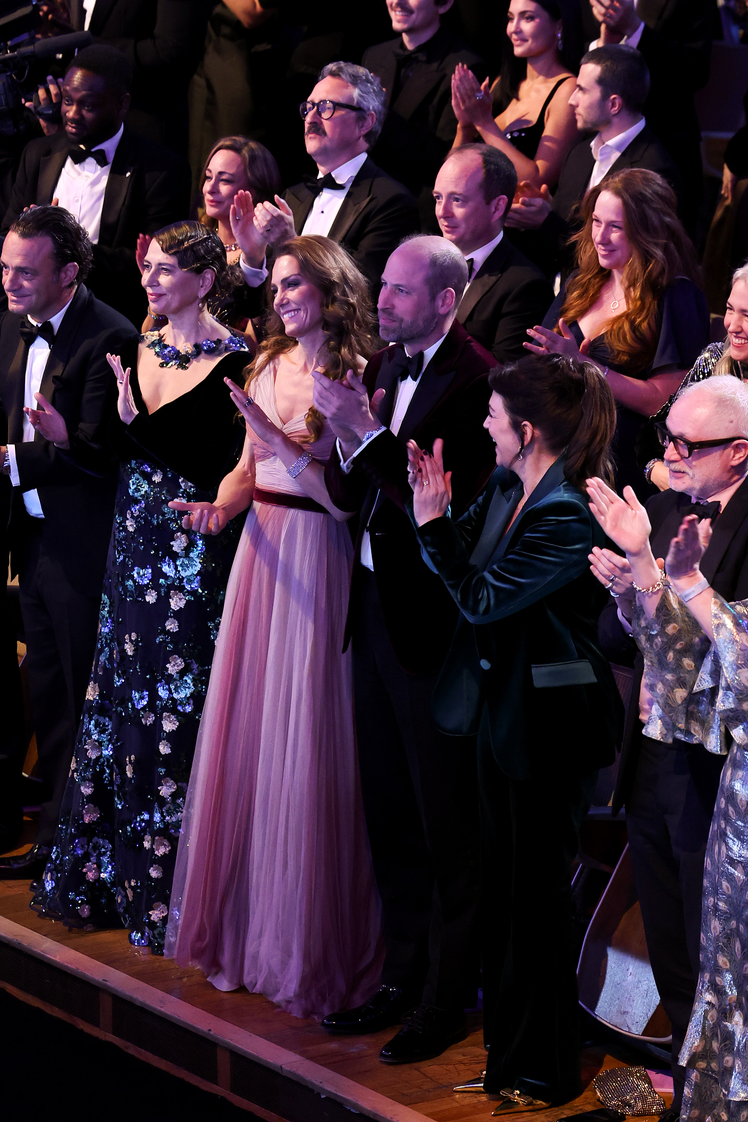 The Prince and Princess of Wales rose to their feet in applause, joining nominees and industry figures in a standing ovation during the 2026 EE BAFTA Awards. Surrounded by a sea of black tie and sequins, the couple clapped in unison, the Princess's maroon waistband and the Prince's velvet jacket subtly linking their formal looks under the stage lights.