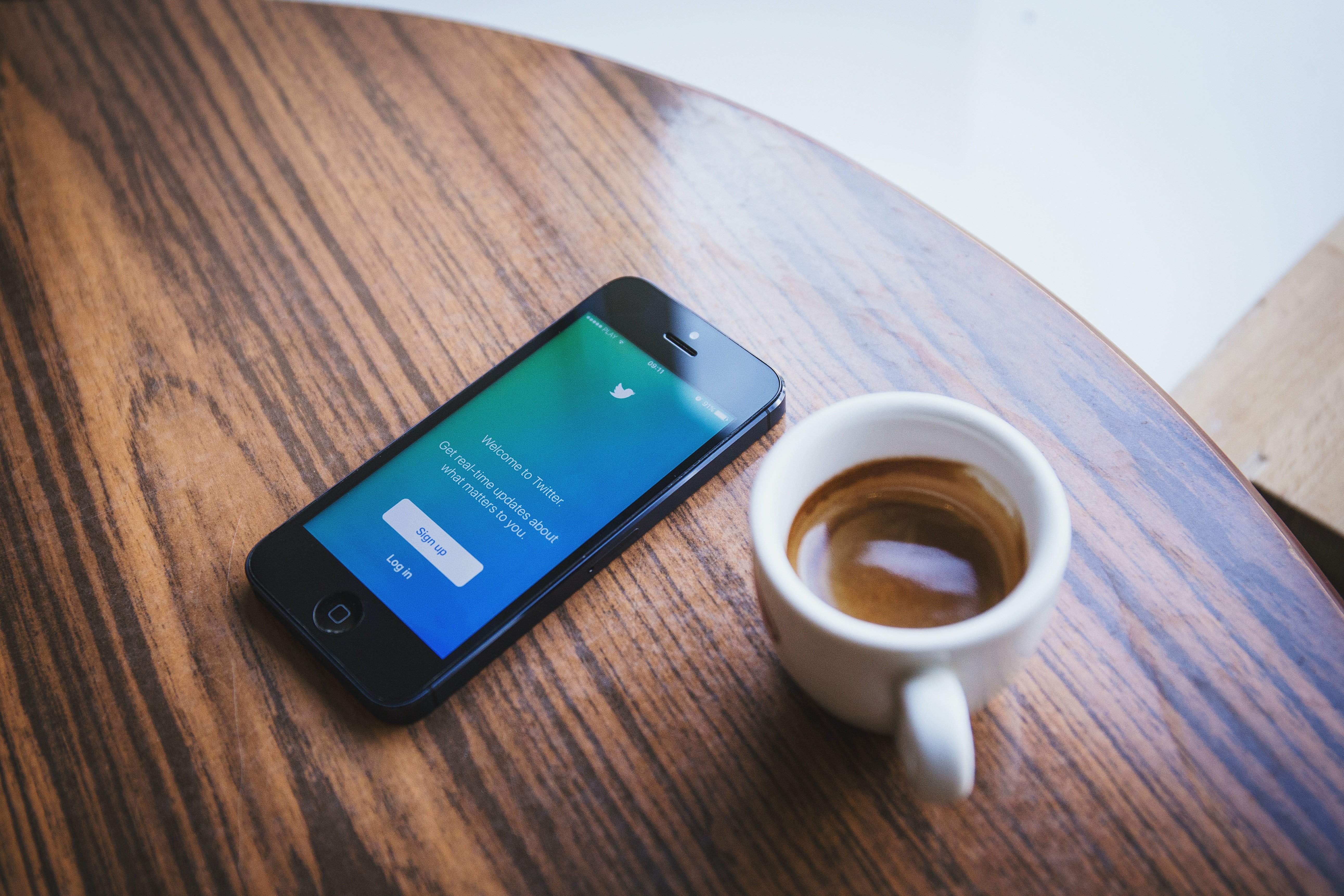 A phone screen is open to Twitter and lies on a table next to a cup of coffee | Photo: Pexels/freestocks.org 
