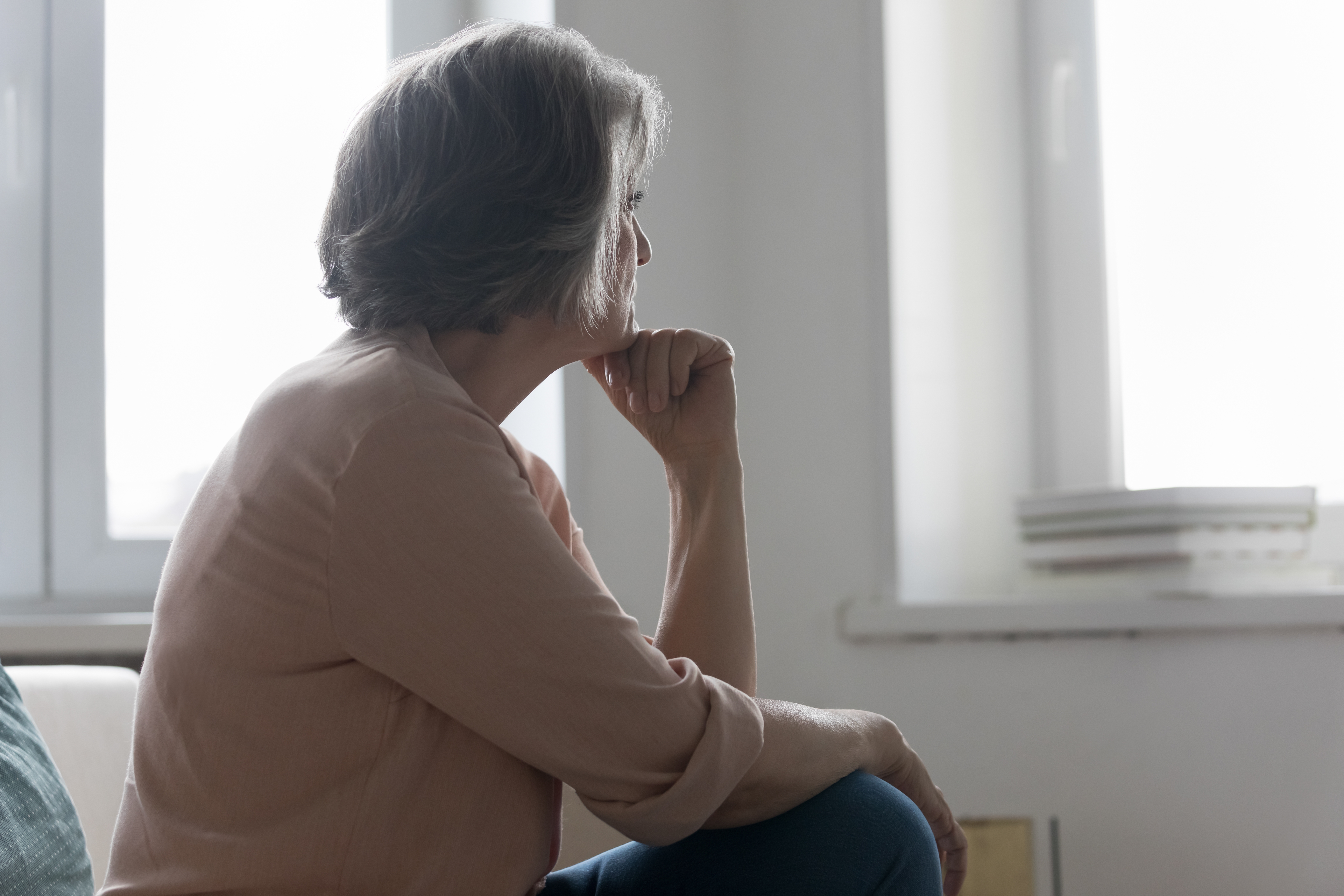 A senior woman wistfully stares at the window while missing someone | Source: Shutterstock