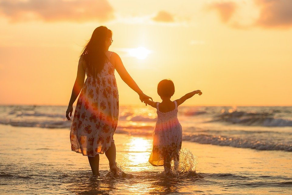 A woman and mother walking on the beach into the sunset. | Photo: Pixabay