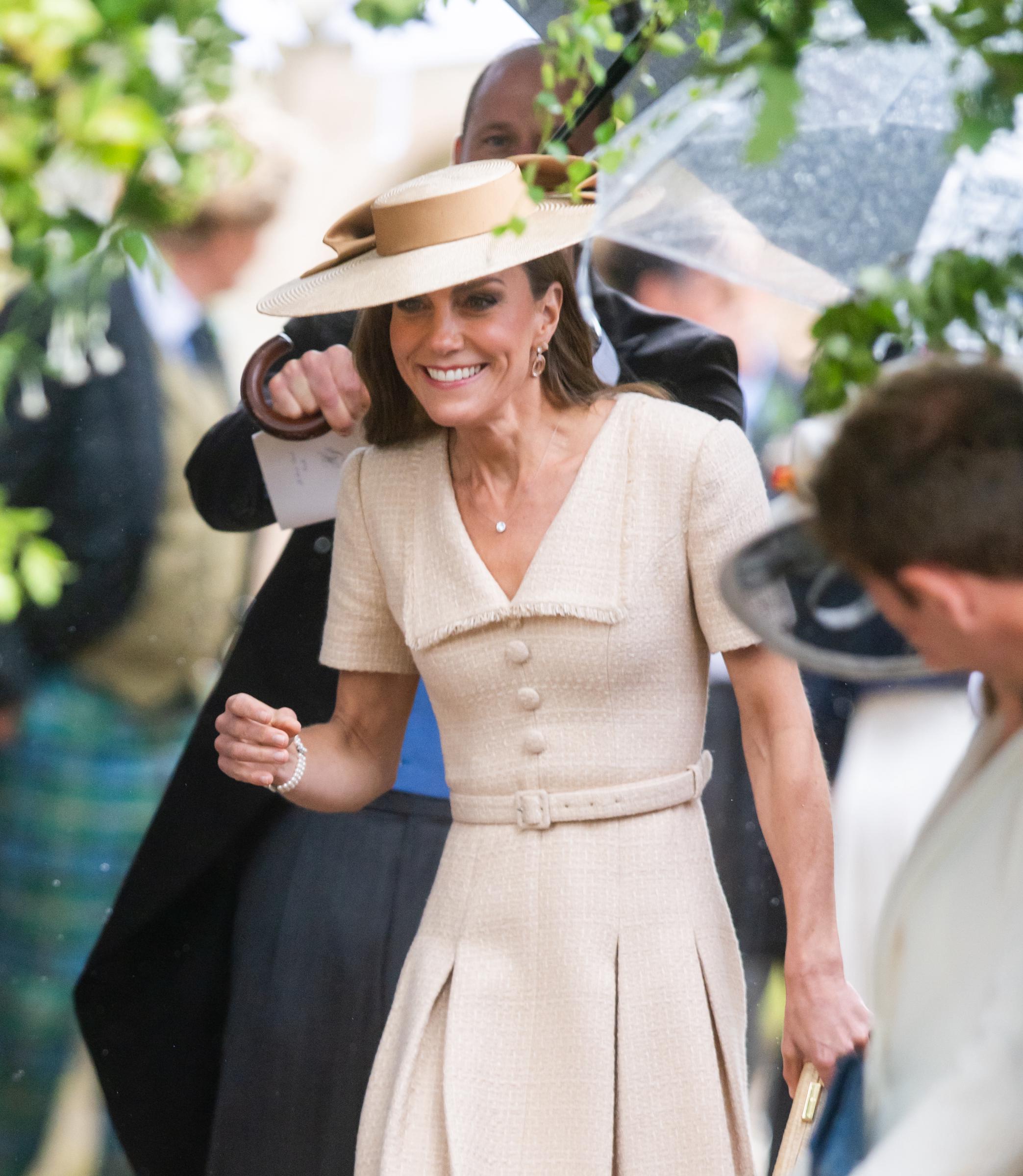 Smiling as she makes her way into the venue, Catherine is pictured beneath an umbrella, with her textured cream dress and coordinating hat standing out against the rainy backdrop. | Source: Getty Images