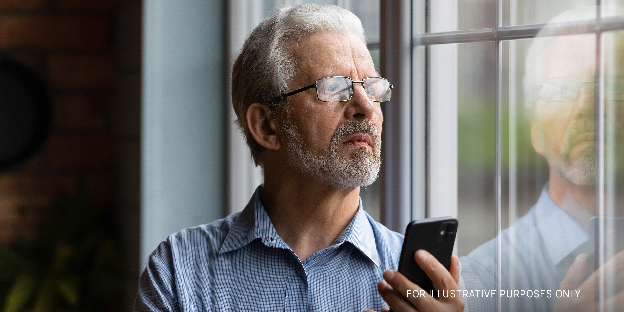 An Older Man Holding a Phone While Standing and Look outside a Window | Source: Shutterstock