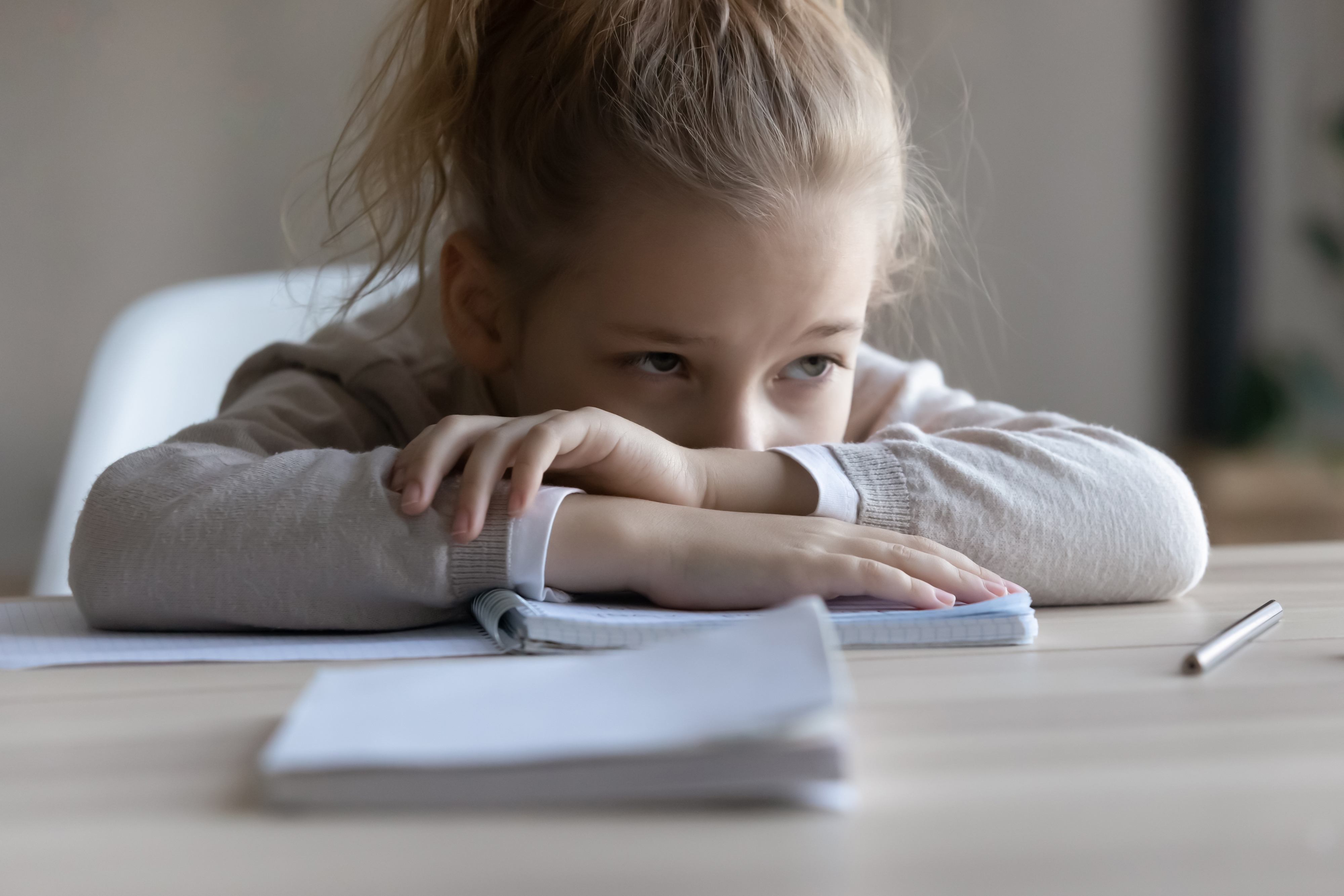 A sad little girl puts her head down on the desk, distracted from work | Source: Shutterstock