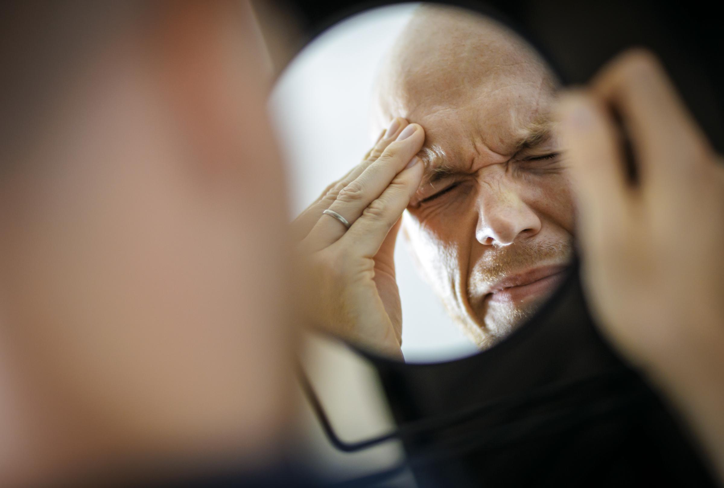 Symbolic image representing migraines and headaches: man holding his aching head in discomfort | Source: Getty Images