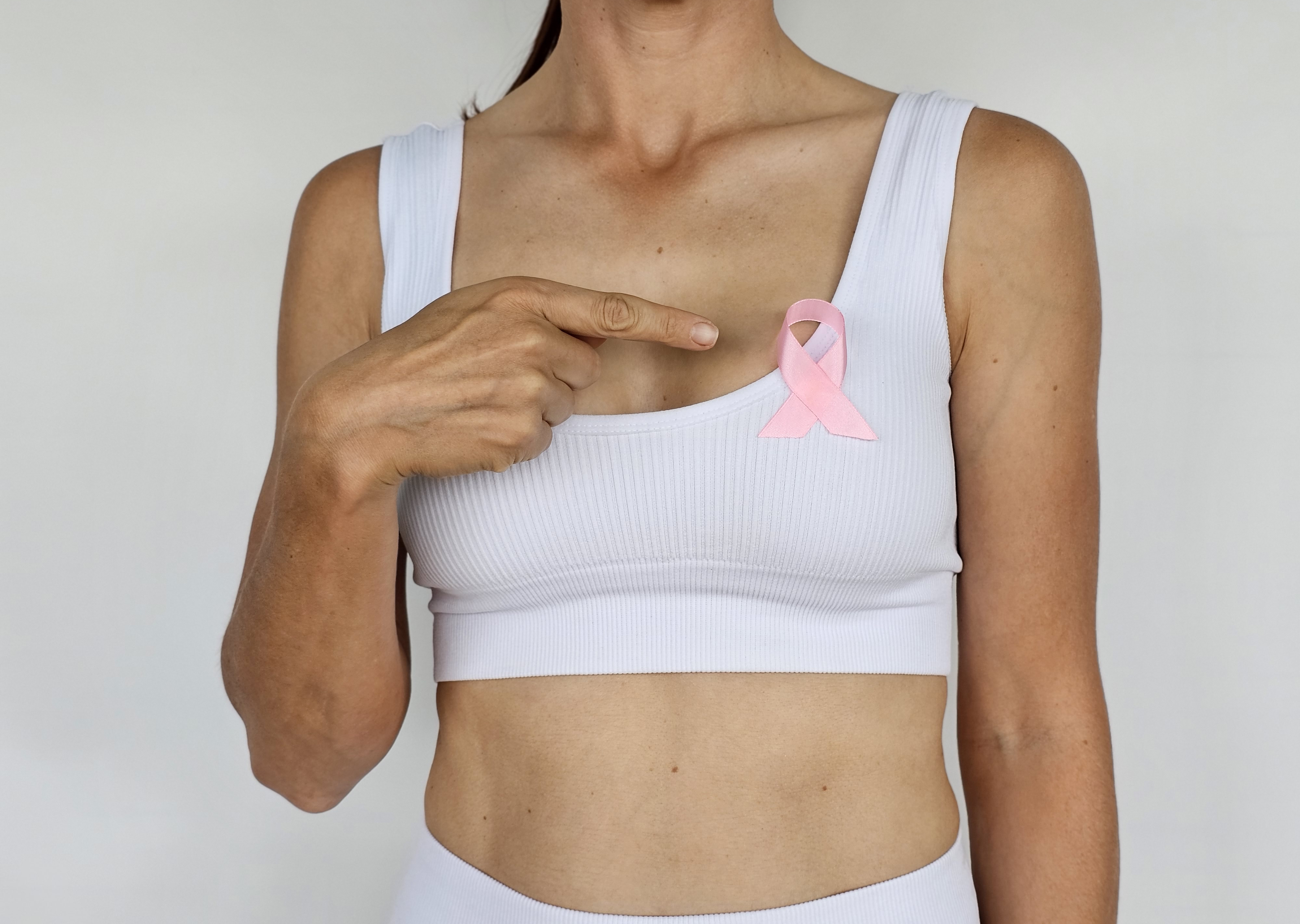 A woman pointing to a pink ribbon pinned to her chest, symbolizing breast cancer awareness | Source: Getty Images