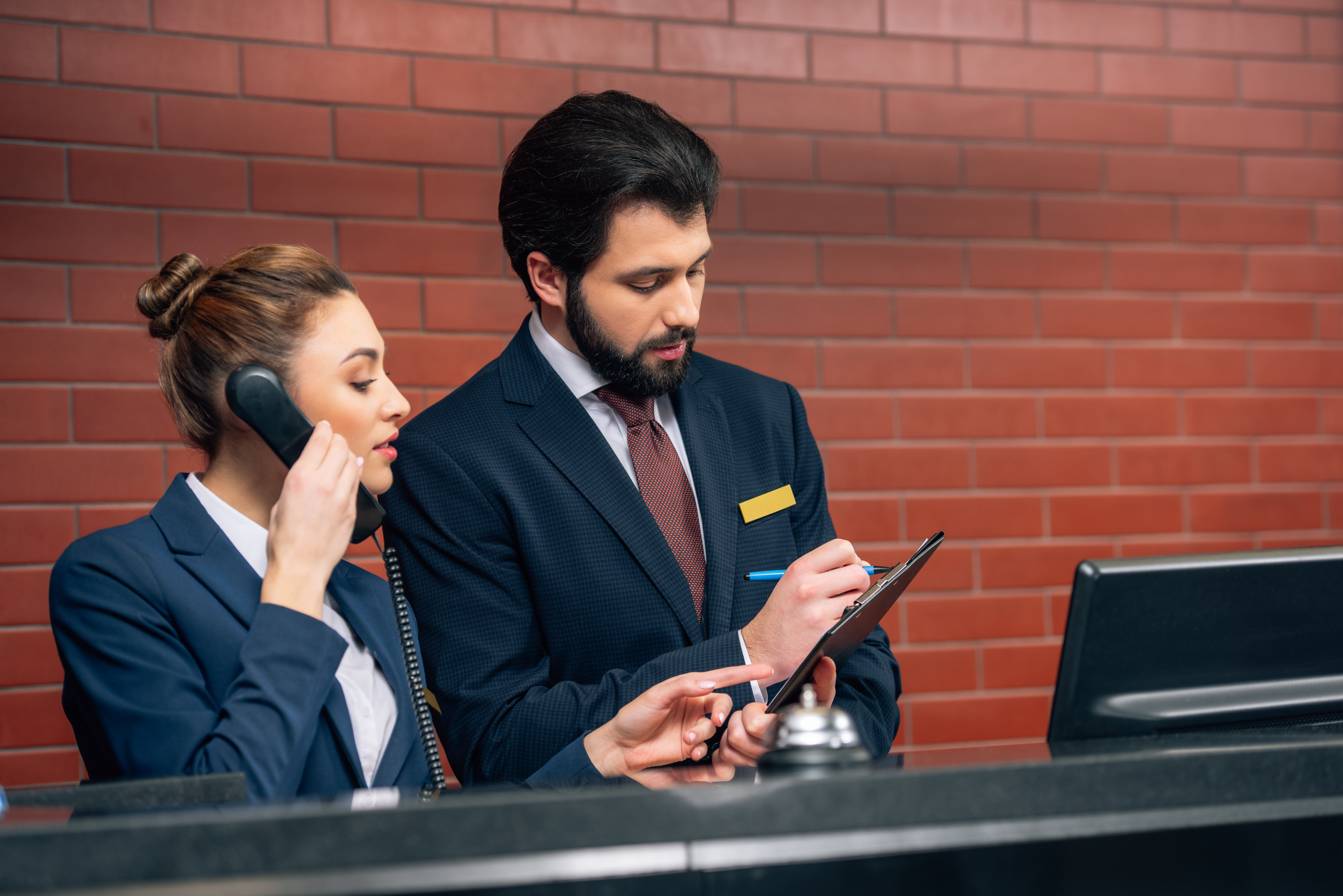 Concentrated hotel receptionists receiving call from customer at workplace. | Source: Shutterstock