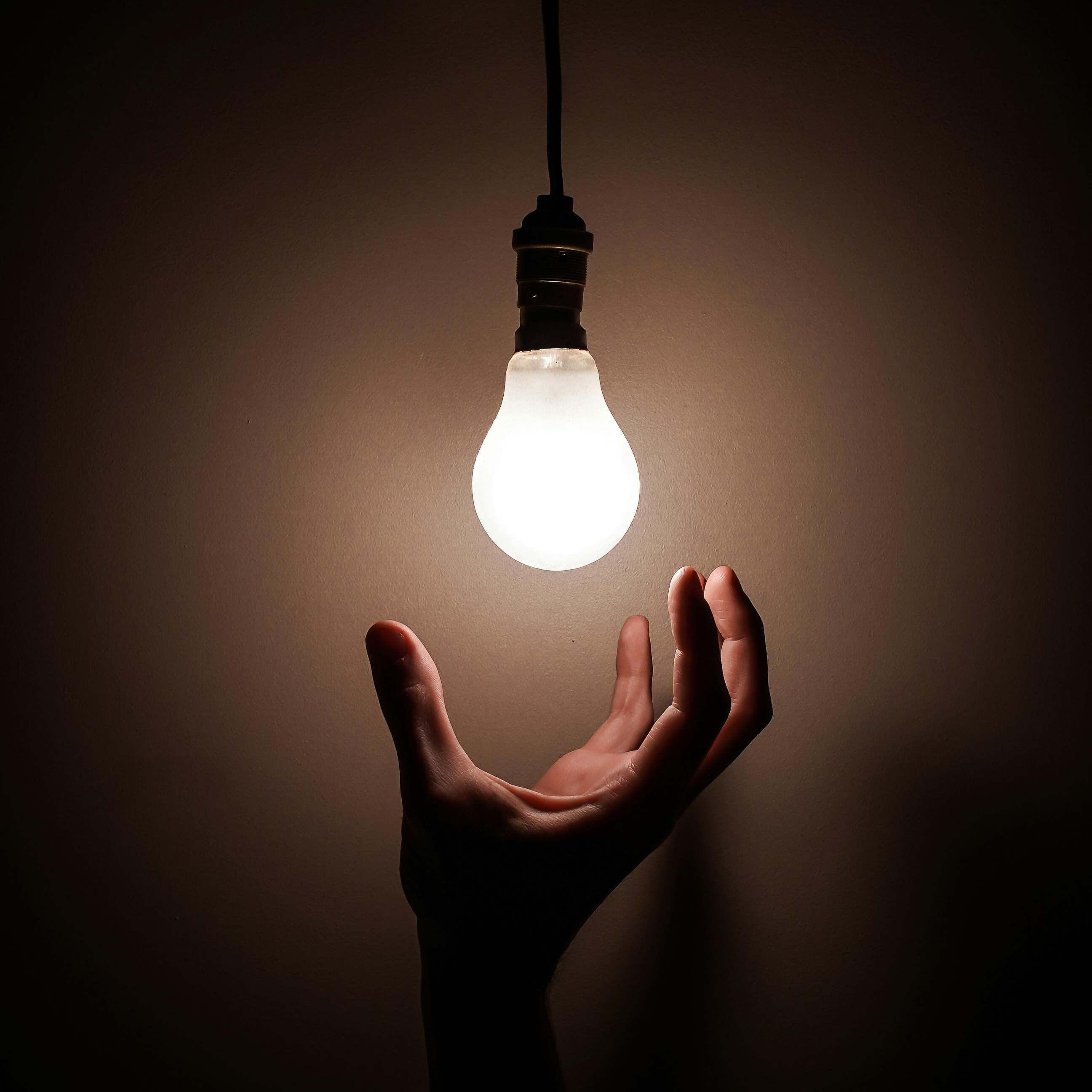 A hand hovering below a lit light bulb | Source: Pexels