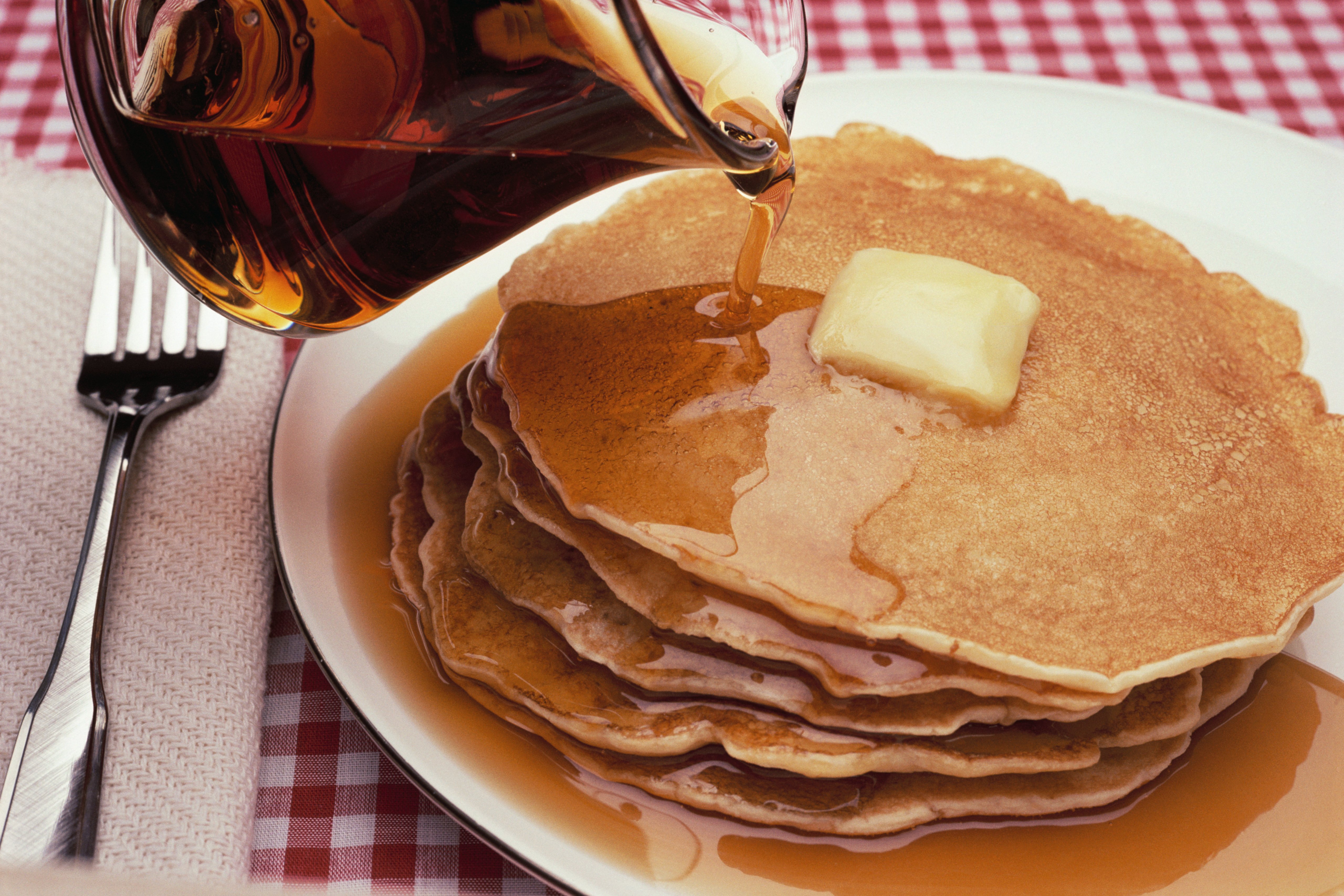 An image of maple syrup being poured on a plate of pancakes | Source: Getty Images