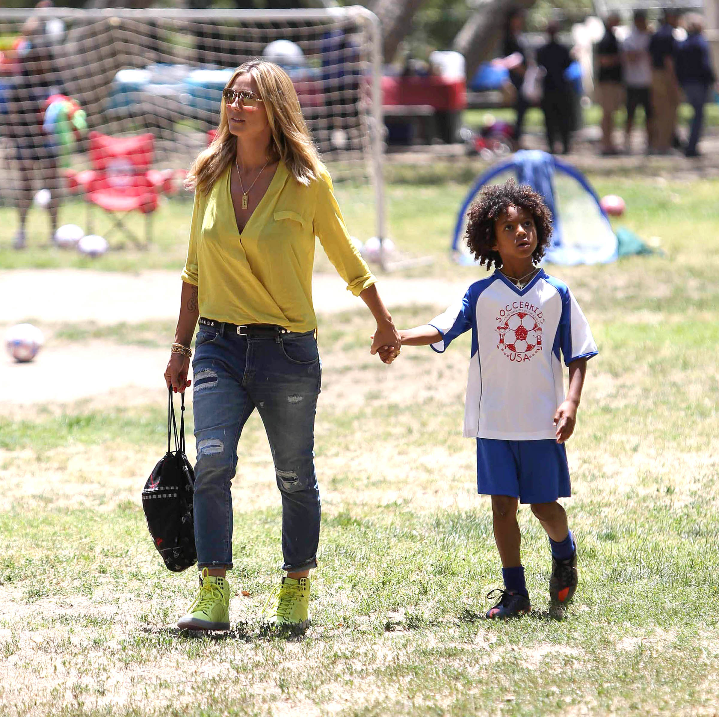 Hand in hand beneath the California sun in Los Angeles, Heidi Klum strolls beside Henry Samuel, who looks up mid-step in his soccer kit.
