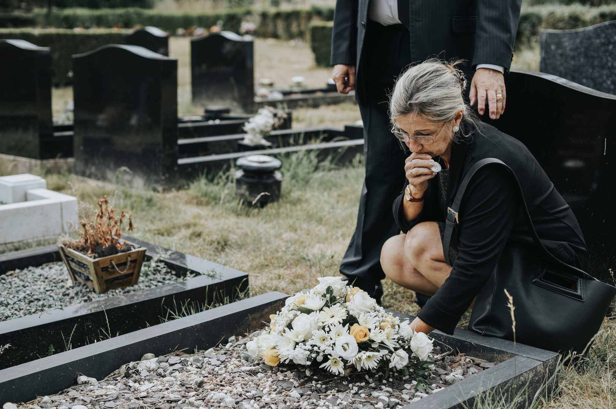 An older woman puts flowers on the grave | Source: Shutterstock