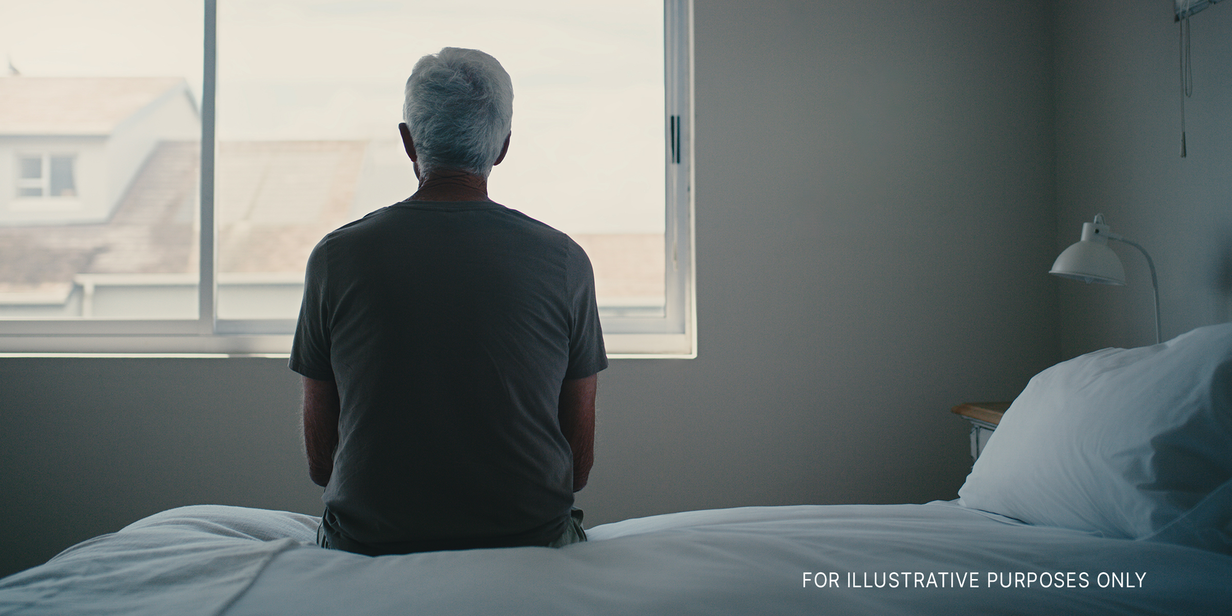 A man sitting on a bed looking out a window | Source: Shutterstock