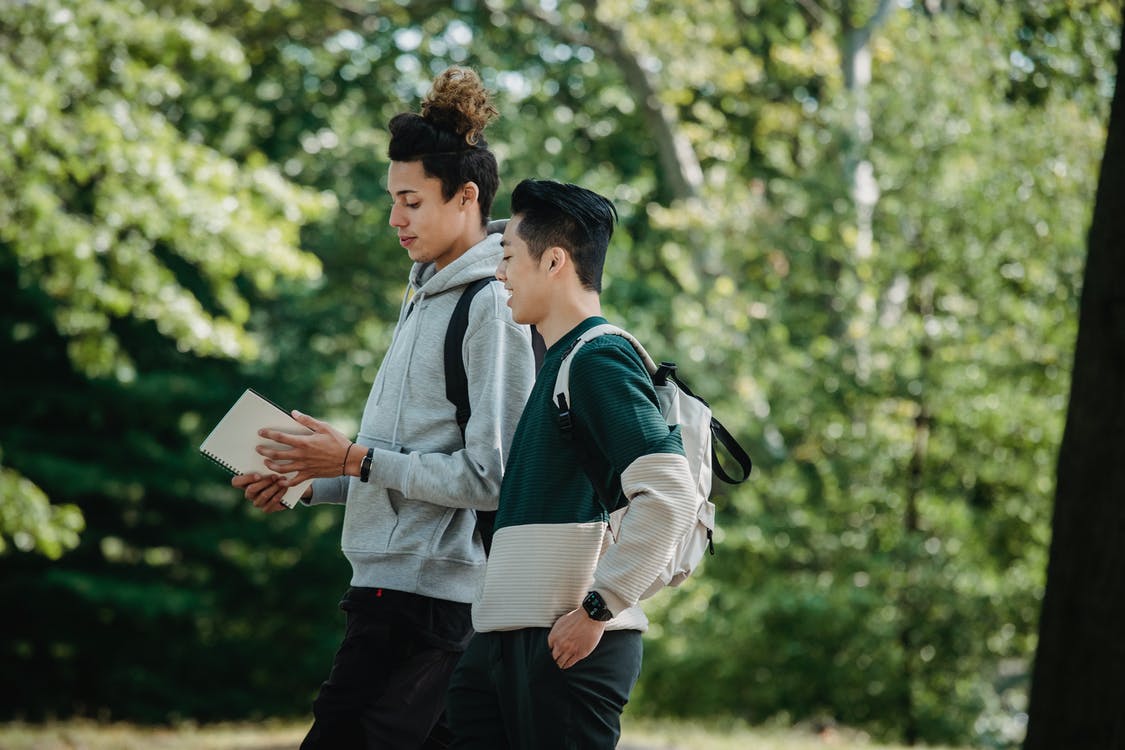 Two students walking with trees in the background | Source: Pexels