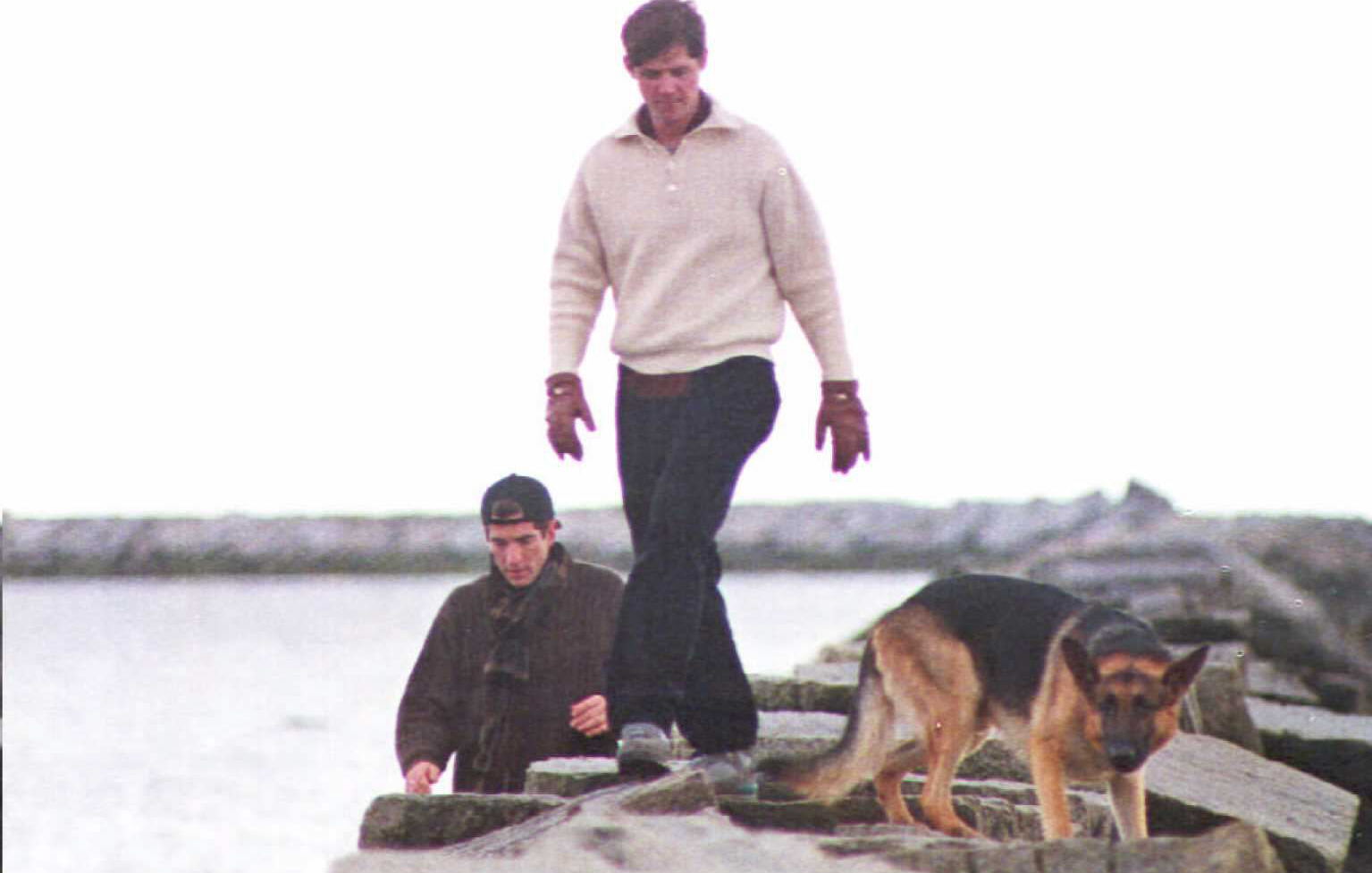 John F. Kennedy Jr. (L), William Kennedy Smith (C), and JFK Jr.'s dog Sampson (R) walking along a breakwater on the family compound in Hyannisport on January 23, 1995 | Source: Getty Images