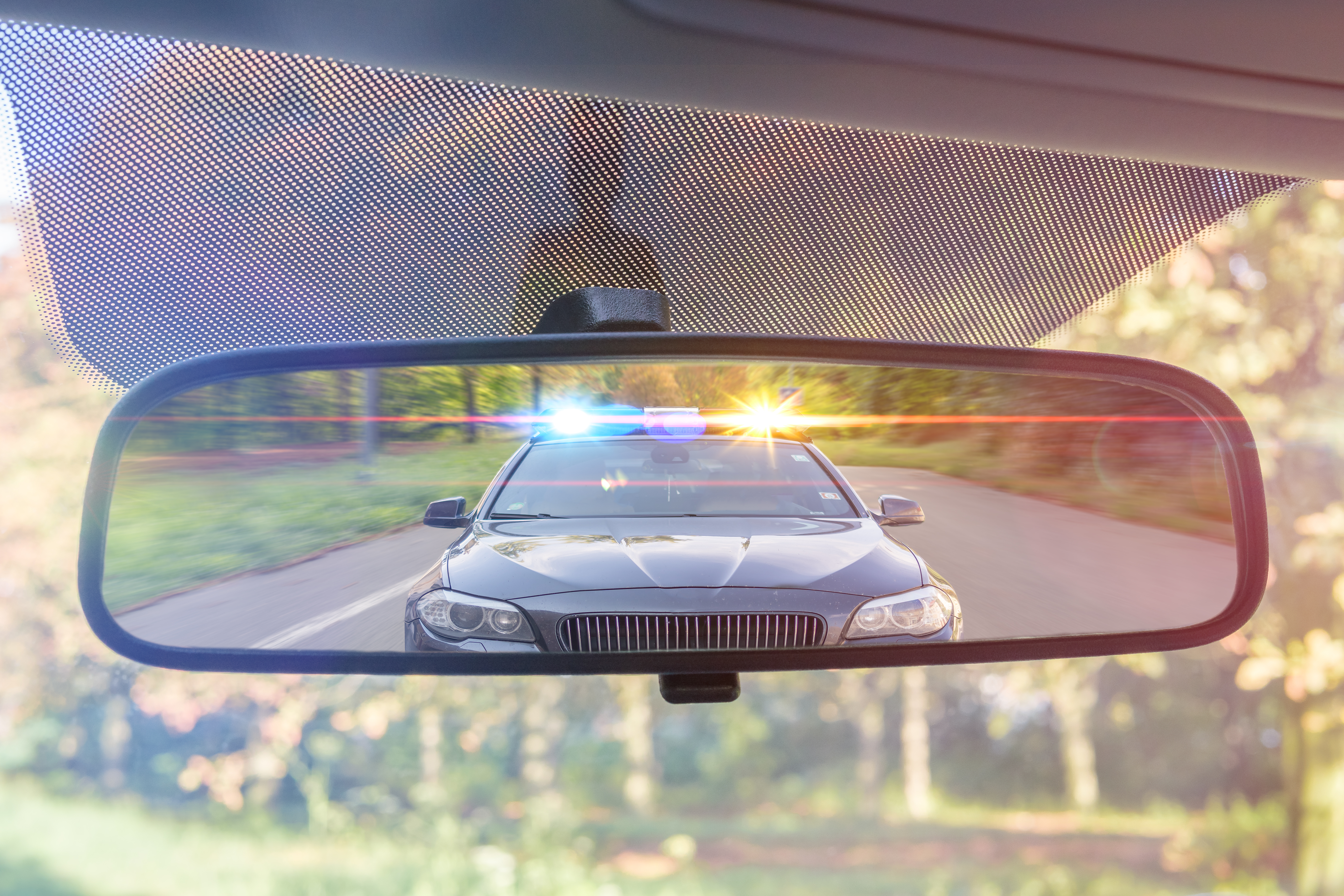 View on rear mirror of a car. Police car with lights and siren is chasing you. | Source: Shutterstock