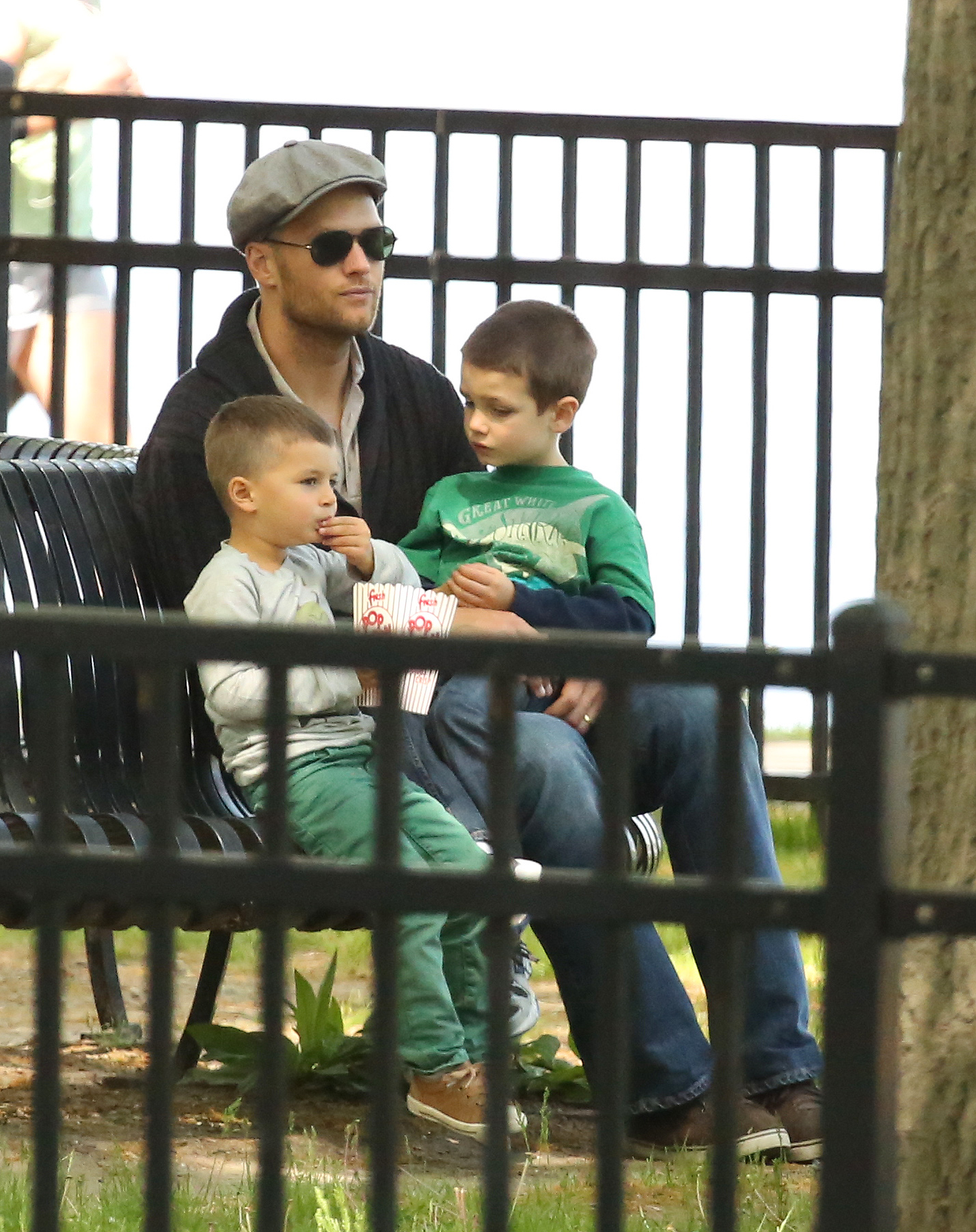 Tom Brady enjoys a quiet afternoon in Boston with sons Jack Moynahan and Benjamin Brady. Little Benjamin enjoys some popcorn as the trio sit on a park bench while soaking in the simple family moment.