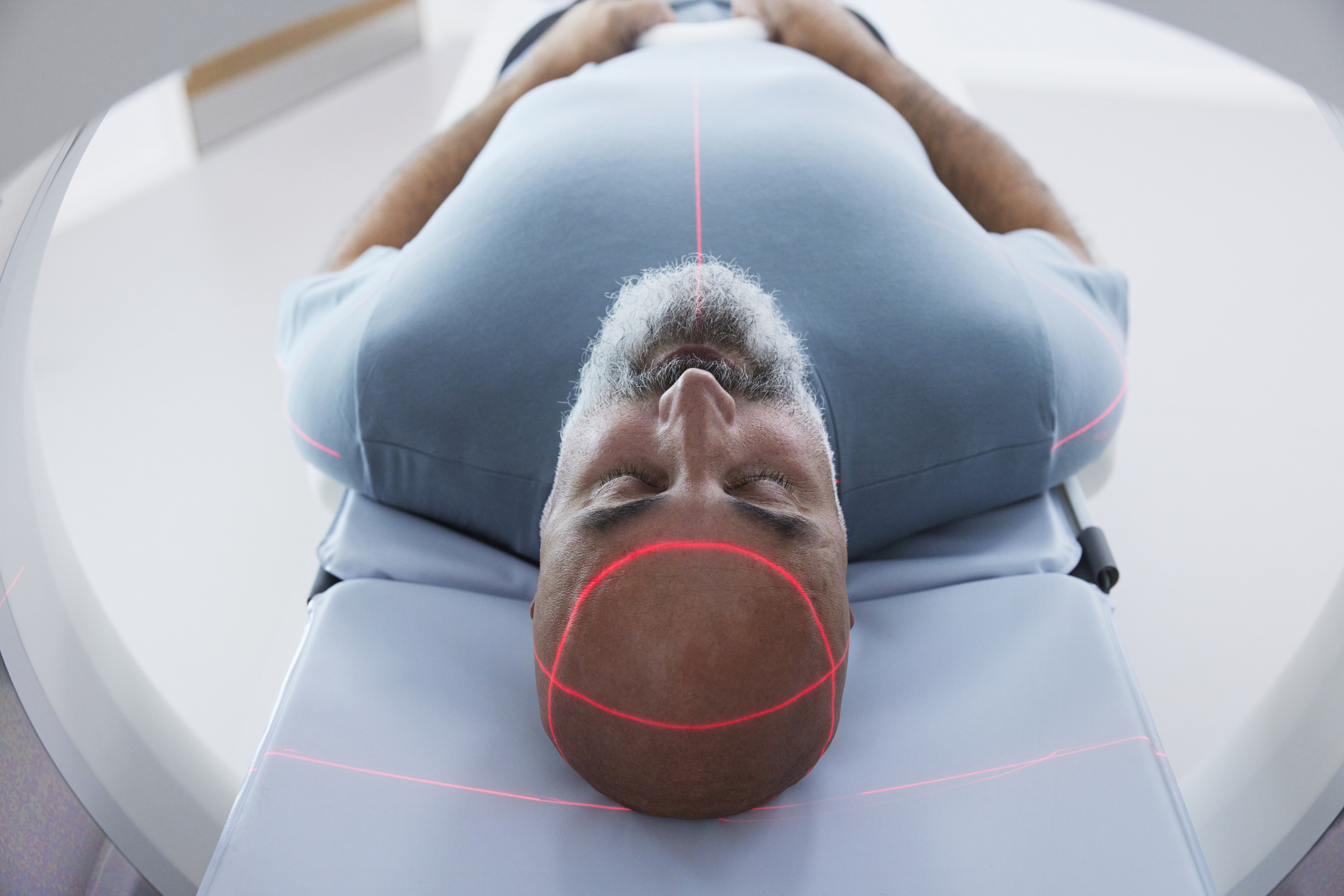 Man undergoing a brain scan inside a CT or MRI machine, with red lasers ensuring proper alignment for detecting tumors or other abnormalities | Source: Getty Images