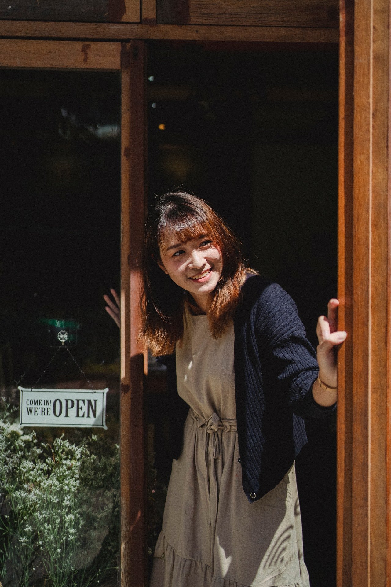 Una mujer sonriente asomada en la puerta de un local. | Foto: Pexels