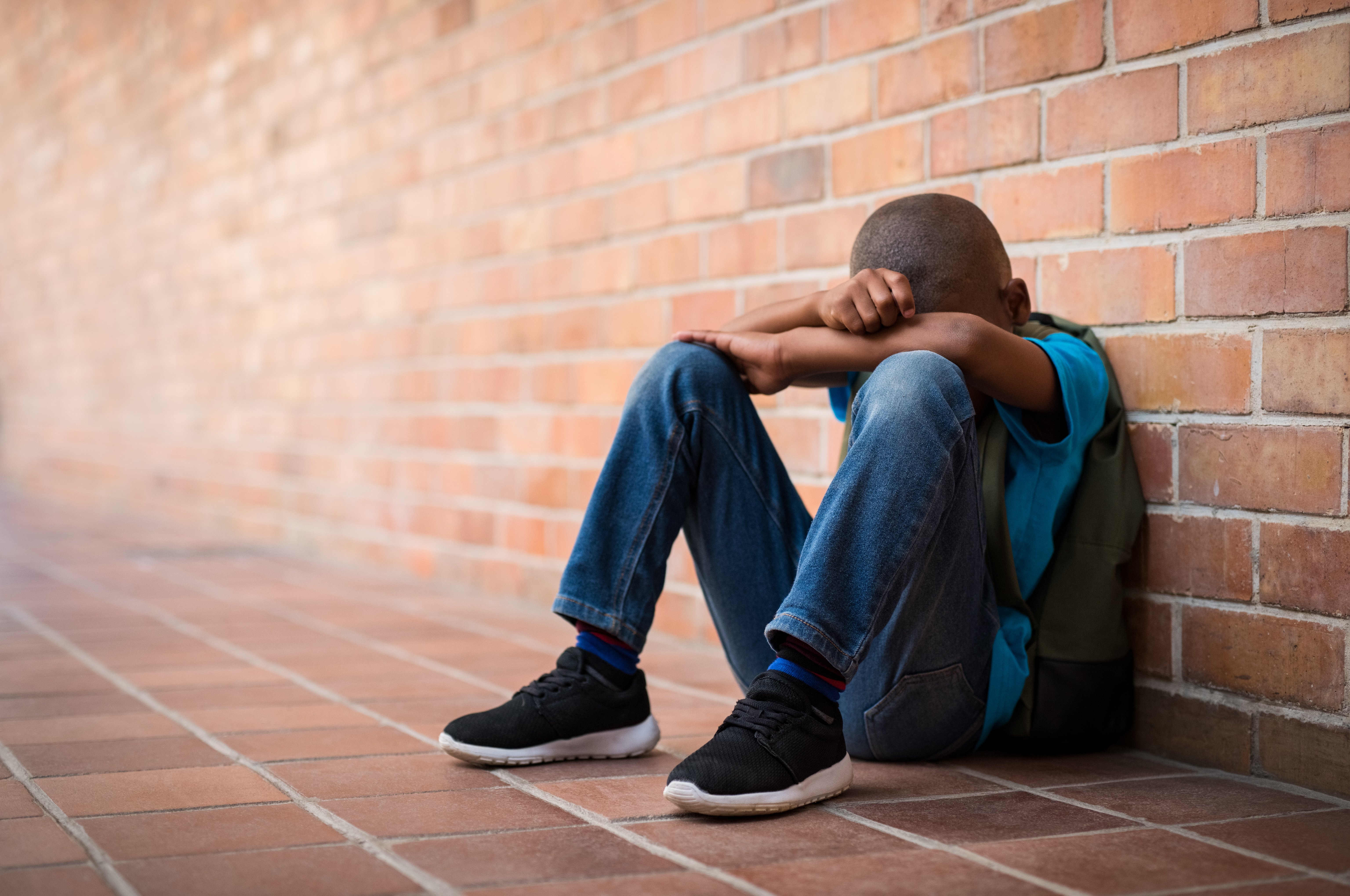 Picture of a sad young boy sitting in an empty brick corridor | Source: Shutterstock