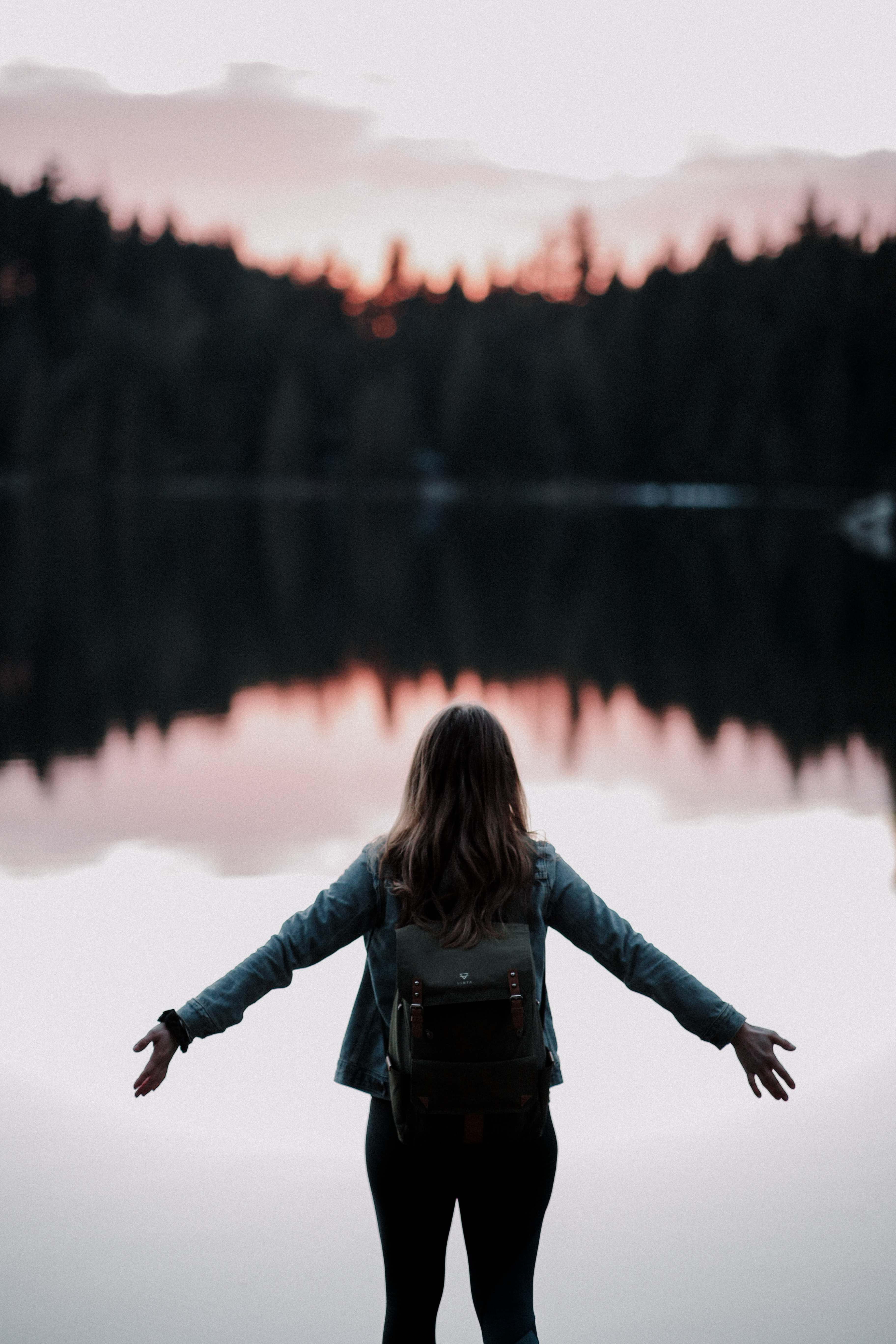 A woman with her arms spread wide open over a lakeside. │Source: Unsplash