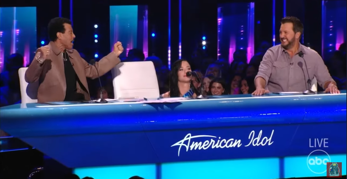 A screenshot shows Katy Perry hiding behind the table after her stylish top snaps during the "American Idol" show.