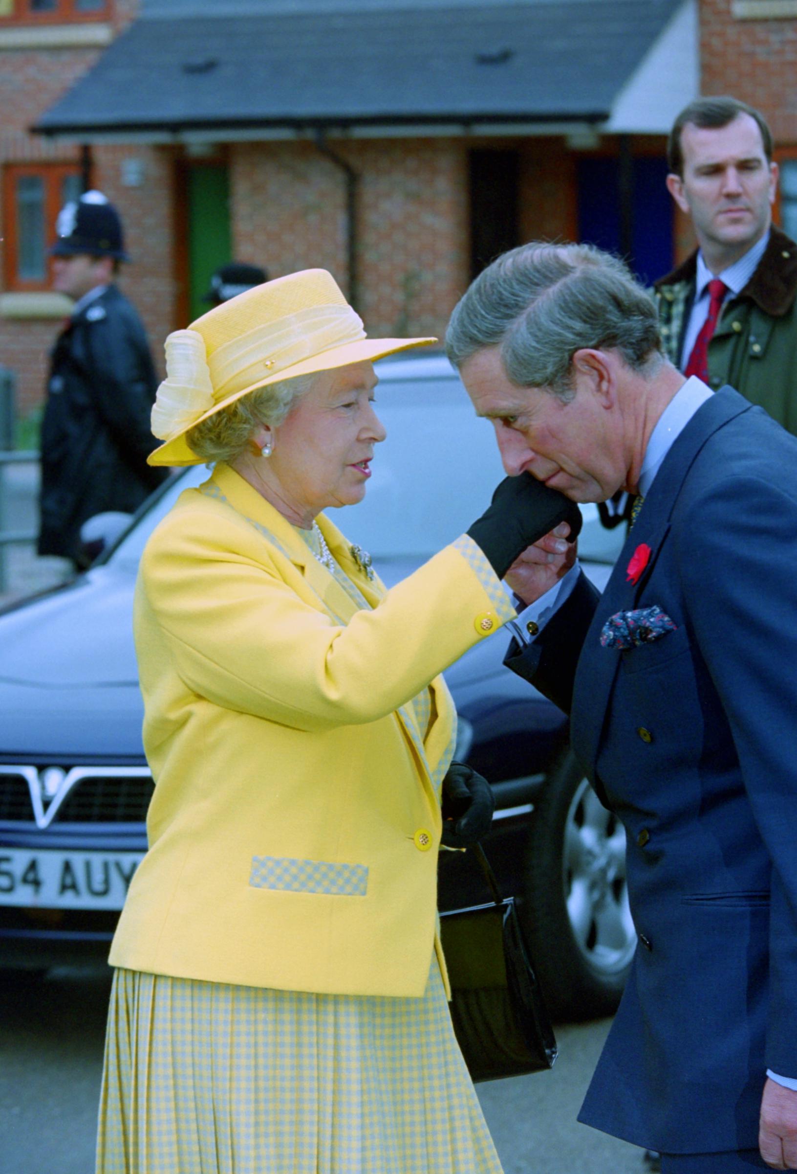 During a visit to a Prince's Trust project in Shepherd's Bush, London, on 11 January 1999, Prince Charles is seen gently kissing Queen Elizabeth II's gloved hand, a gesture of respect and affection that reflects both their personal bond and the enduring sense of duty shared between mother and son.