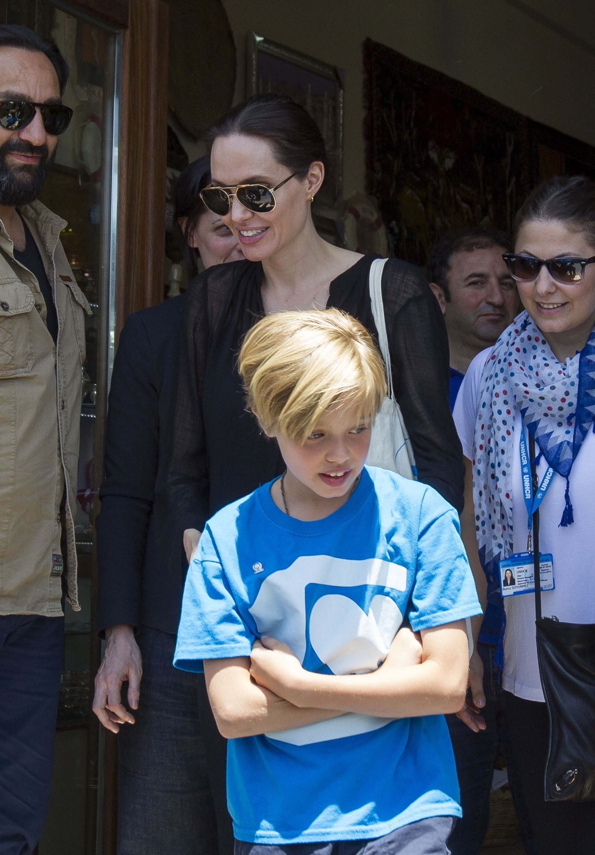 Angelina Jolie visits Mardin, Turkey, with Shiloh Jolie-Pitt during a humanitarian trip. In a simple blue T-shirt, Shiloh walks ahead, her look casual and unguarded. The moment reflects a quieter side of her upbringing beyond the spotlight.