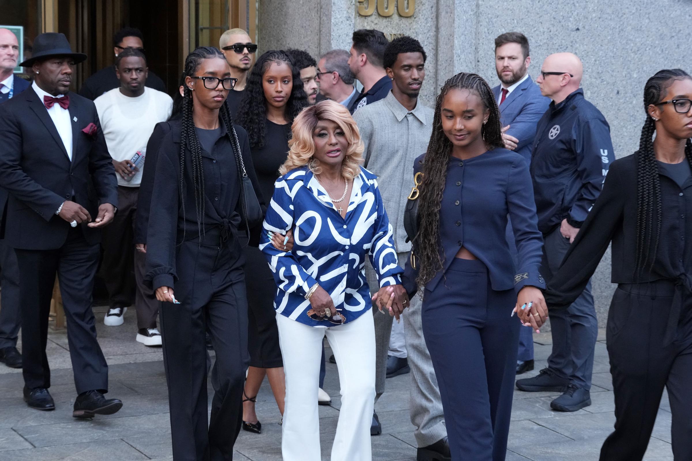 Janice Combs walks out of Manhattan Federal Court with her granddaughters. She holds D'Lila's arm, wearing a serious look. The daughters appear calm, with faint smiles. The family leaves together, showing unity after the verdict.