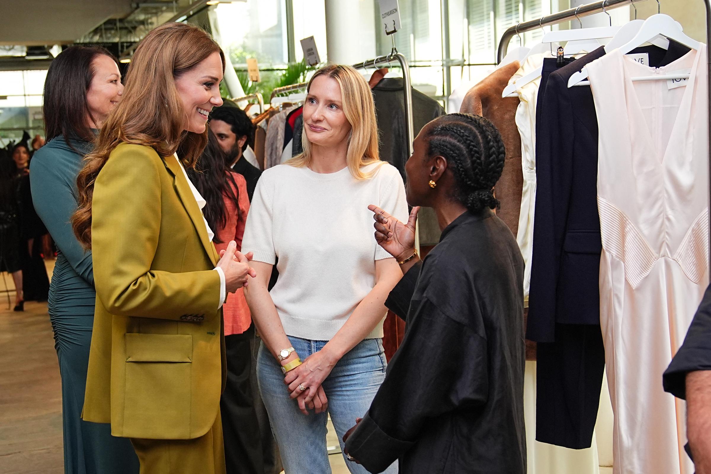 As Catherine views clothing designed by Tove, she listens intently to founders Camille Perry (R) and Holly Wright (C), her attention fully on them, most likely taking in details about their creative process and the inspirations behind their designs.