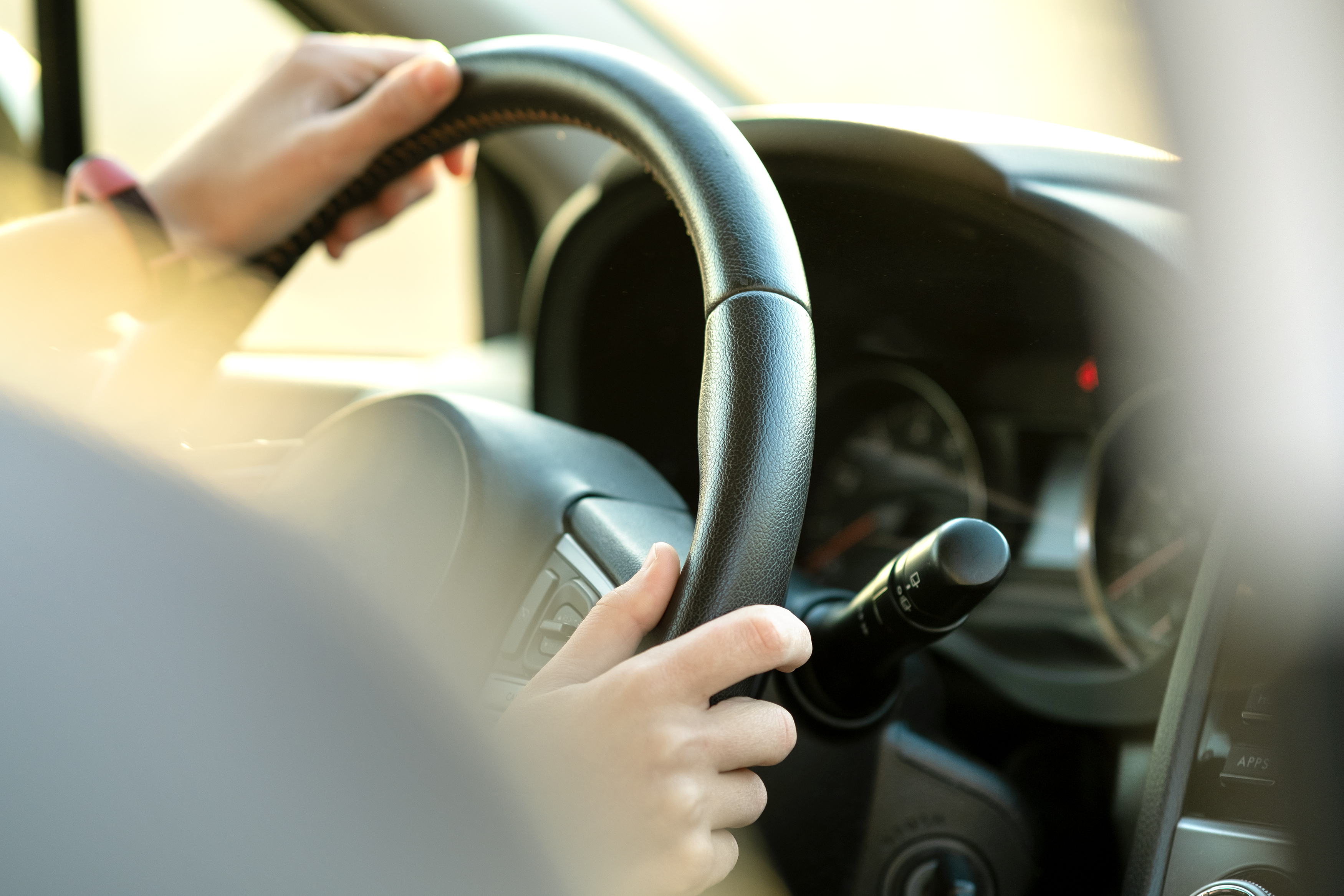 Close up view of woman hands holding steering wheel driving a car on city street on sunny day. | Source: Shutterstock