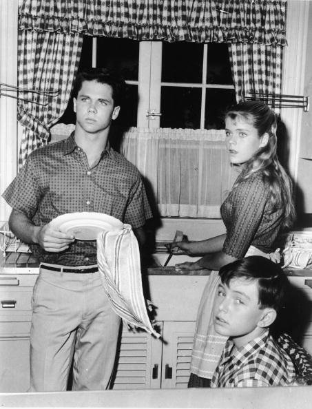 Tony Dow washes dishes with a towel as he stands in the kitchen alongside an unidentified actress and Jerry Matherswho sits and gives the camera a glance, circa 1960. | Source: Getty Images.