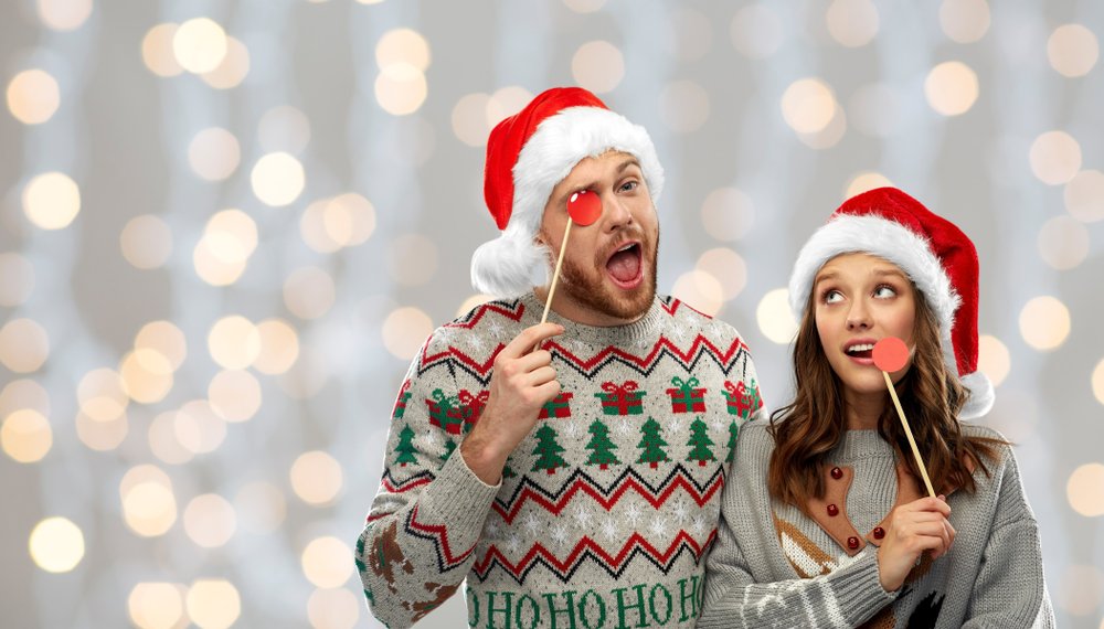 Pareja vistiendo suéteres navideños con luces de fondo. | Foto: Shutterstock