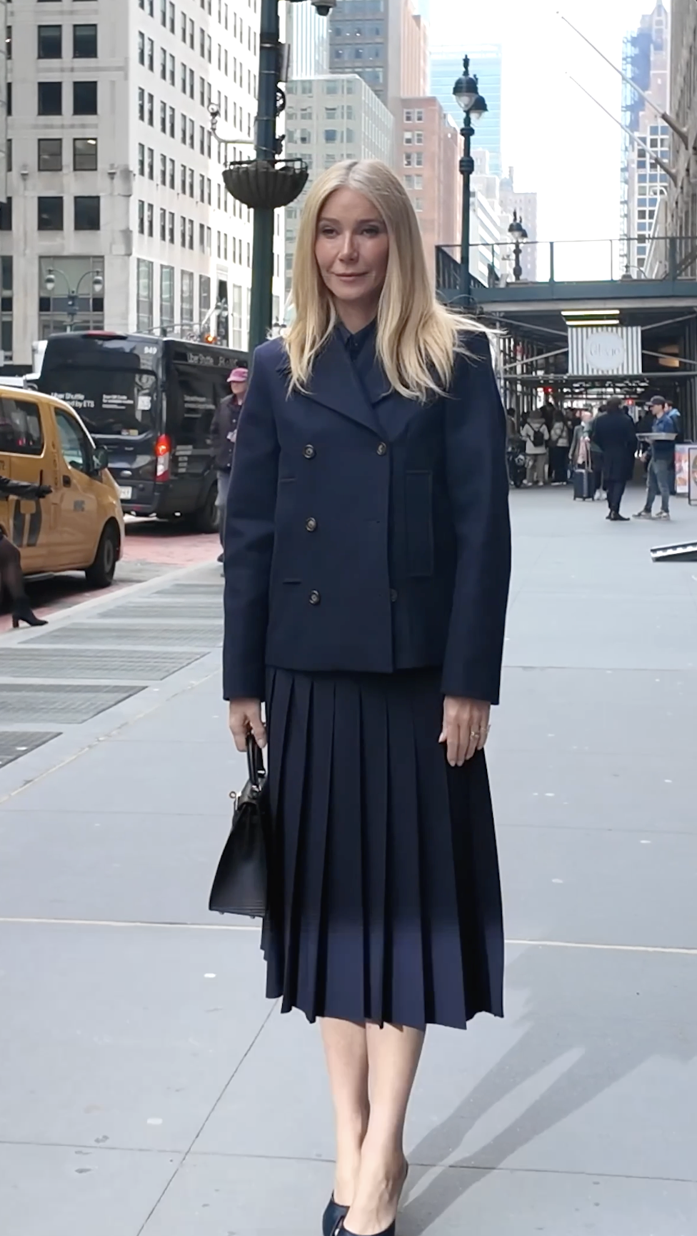Gwyneth Paltrow stands facing forward on a New York street, her posture upright and composed, with the full navy look clearly visible.